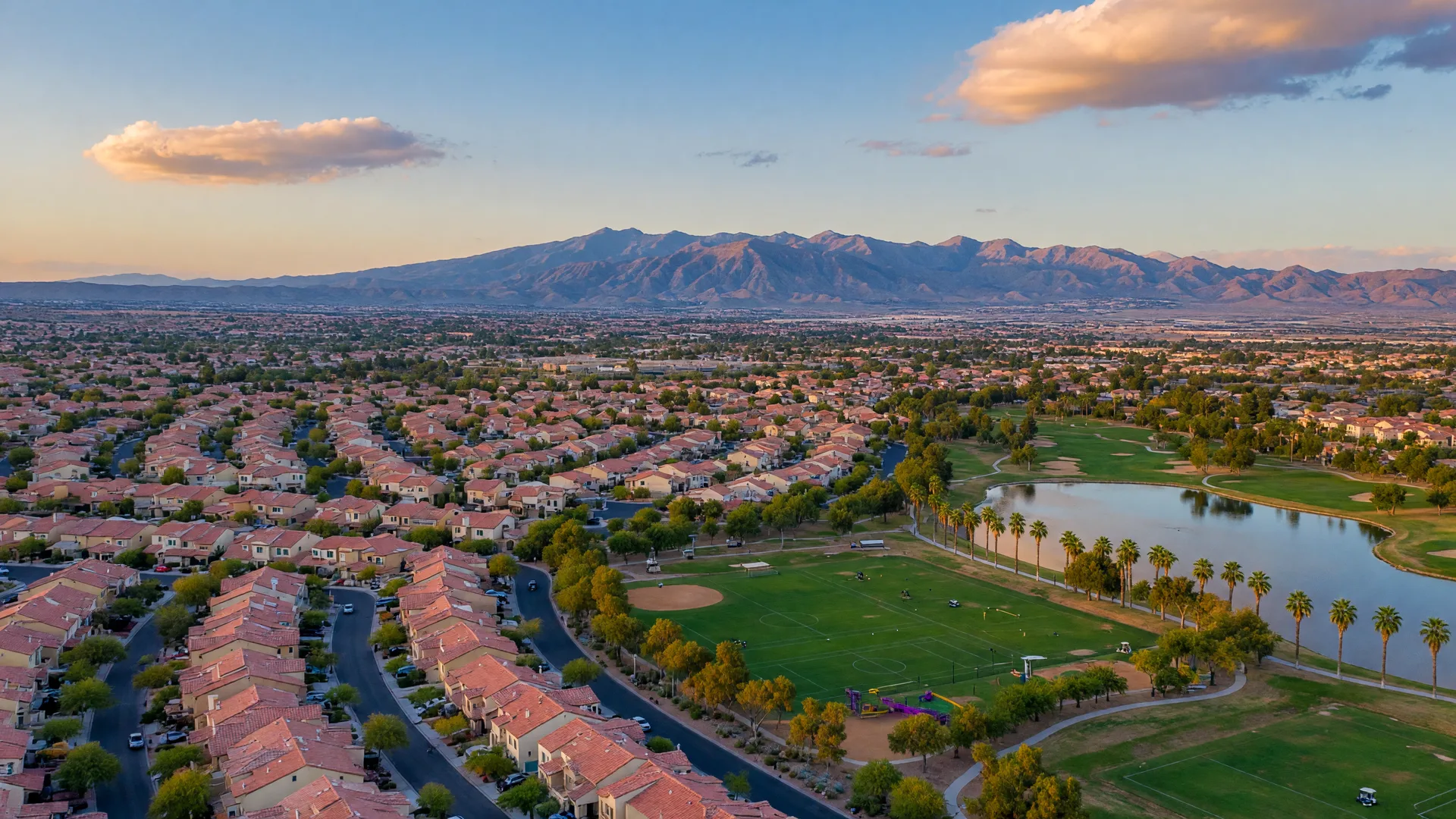 Golden-hour aerial of Southwest Las Vegas master-planned communities in early autumn with parks, a golf course, and the Spring Mountains