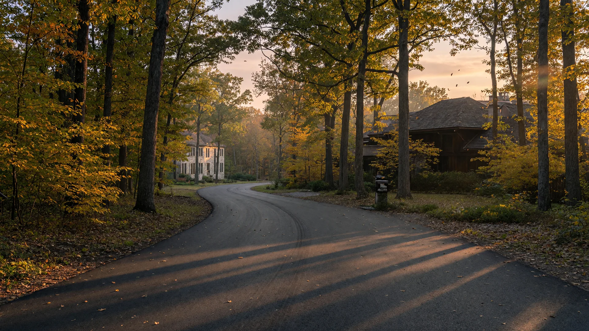 A quiet private road curving through mature Michigan woodlands at golden hour near wooded one-acre homesites in Tyrone Township