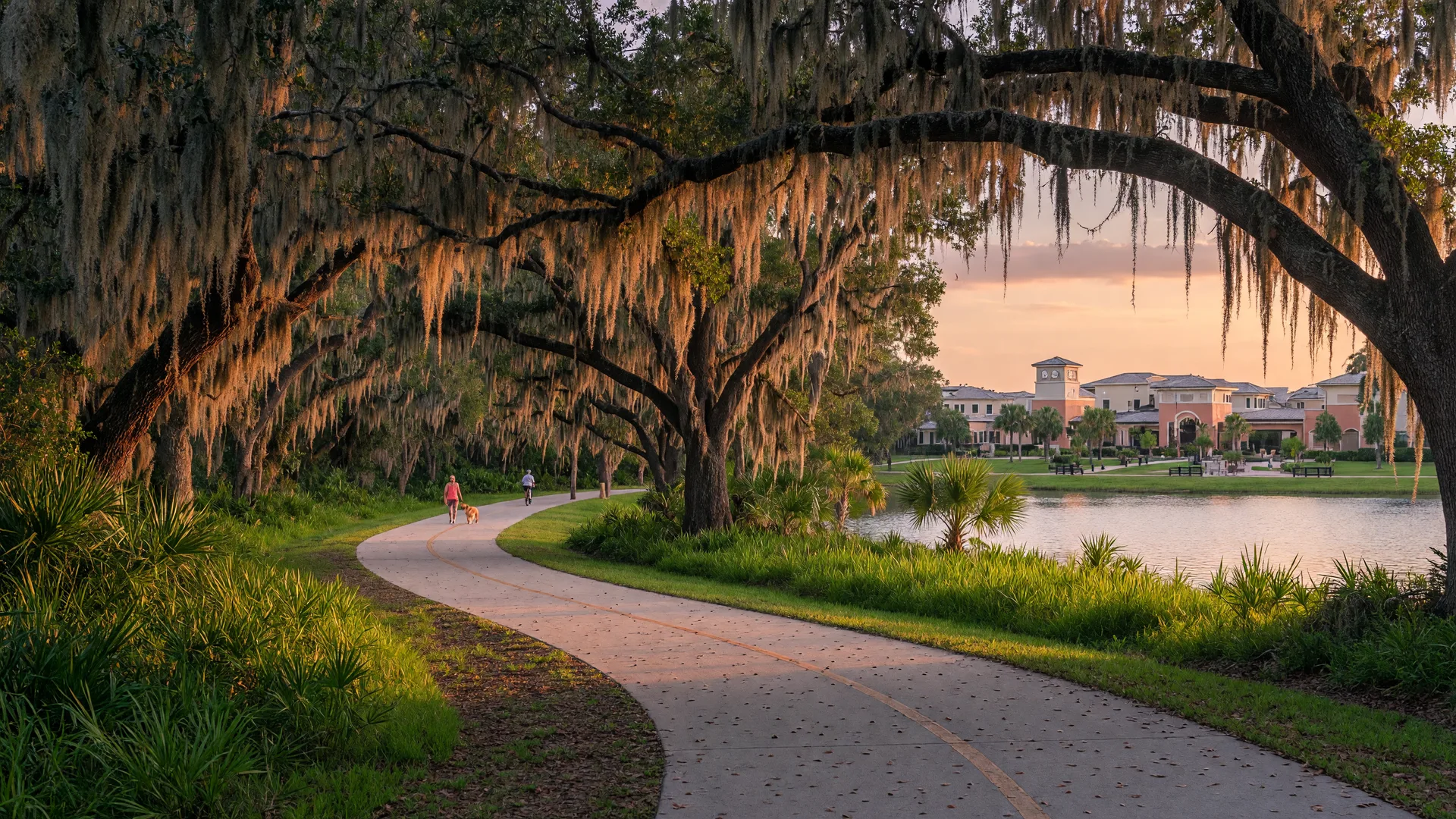 A paved multi-use trail curving through moss-draped oak trees near a lake in Odessa, Florida at golden hour