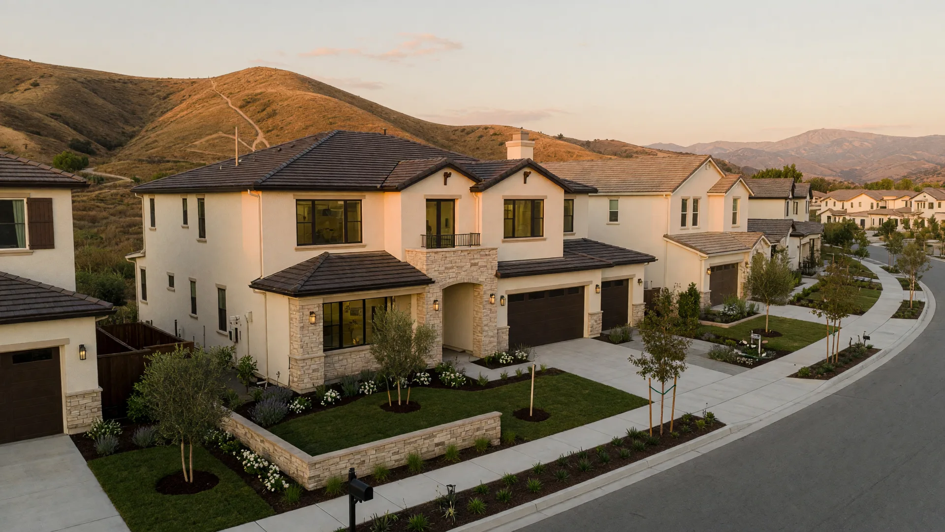 A brand-new luxury home on a tree-lined street in a Southern California master-planned community at golden hour, with rolling hills behind the roofline