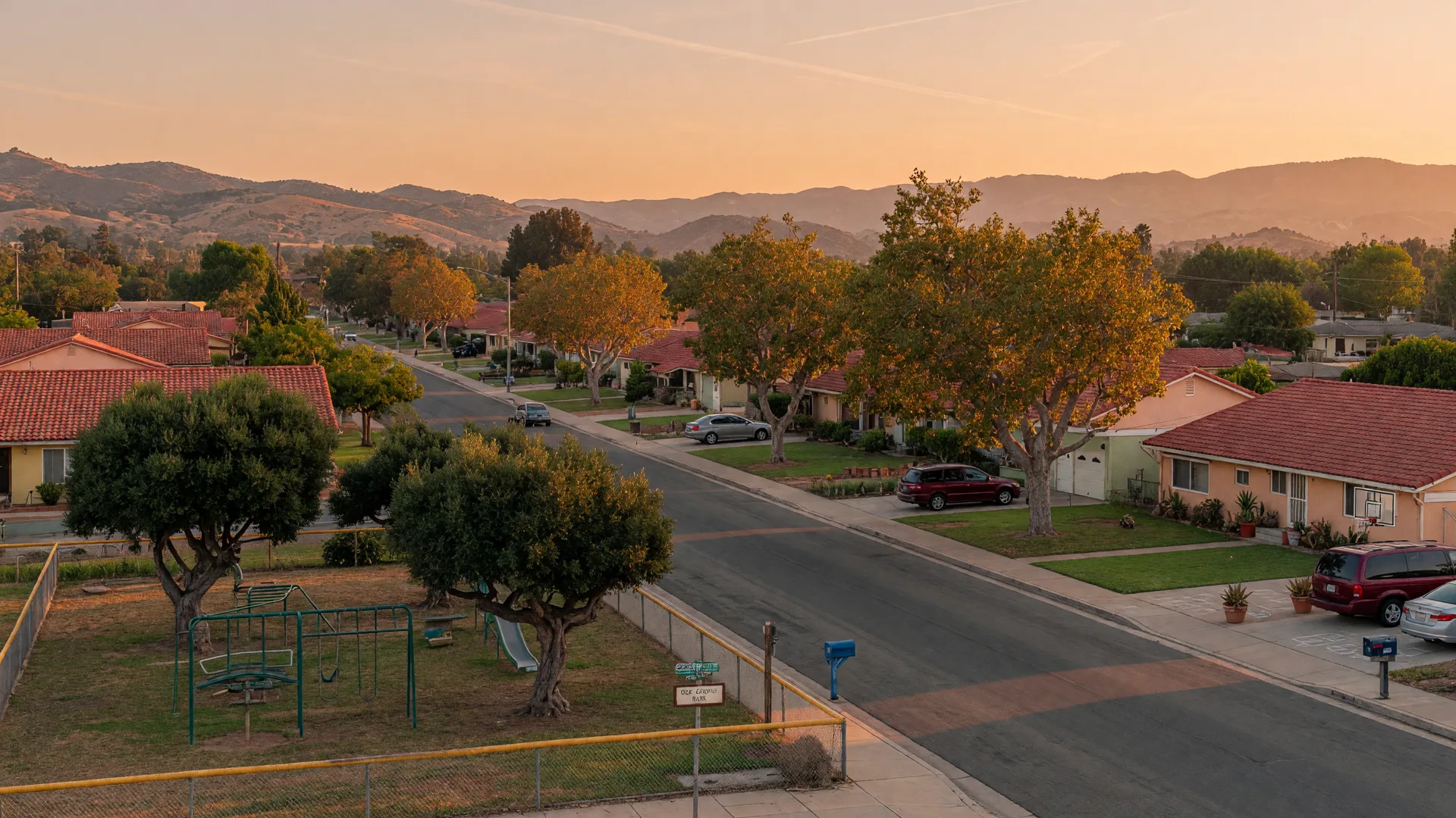 A quiet tree-lined street in a Southern California valley at golden hour, with family homes and a small neighborhood park