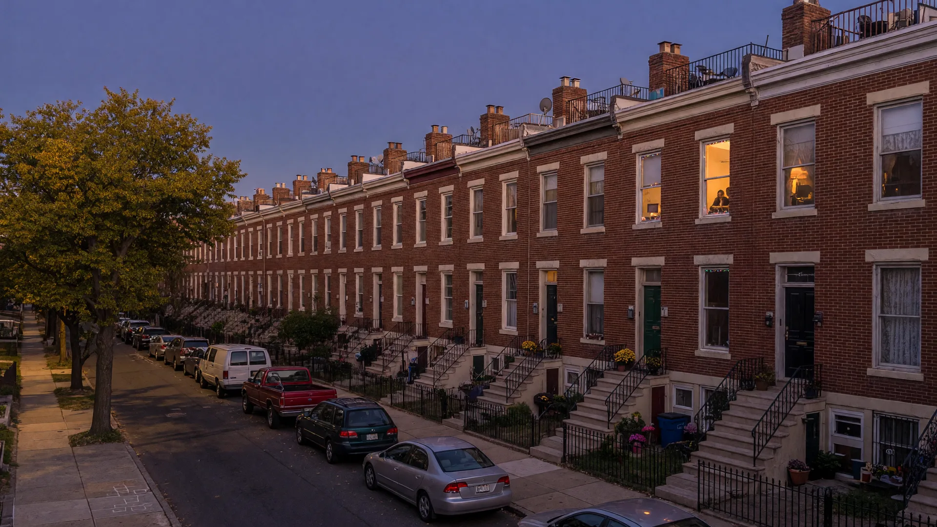 A row of classic brick Philadelphia rowhouses on a tree-lined street at golden hour