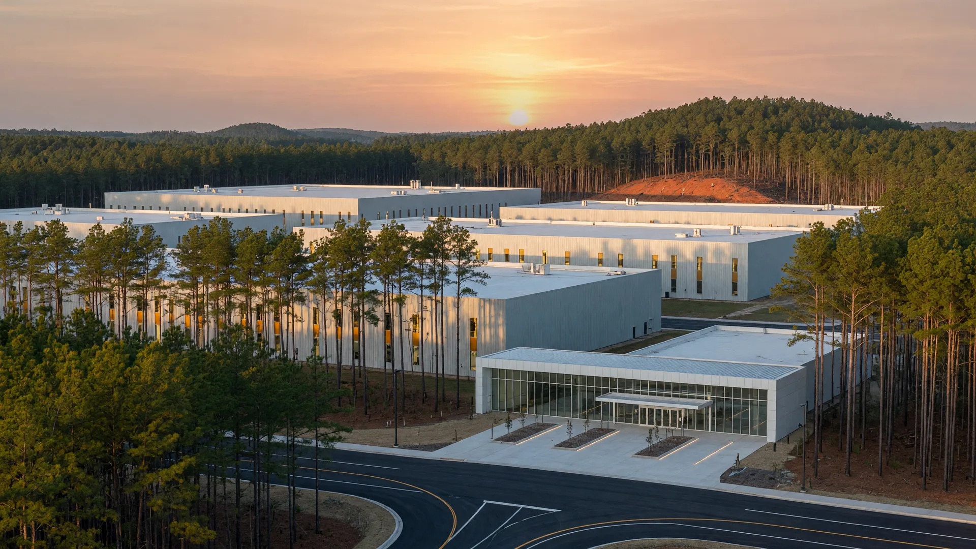 New automotive manufacturing campus rising among Carolina pines at golden hour