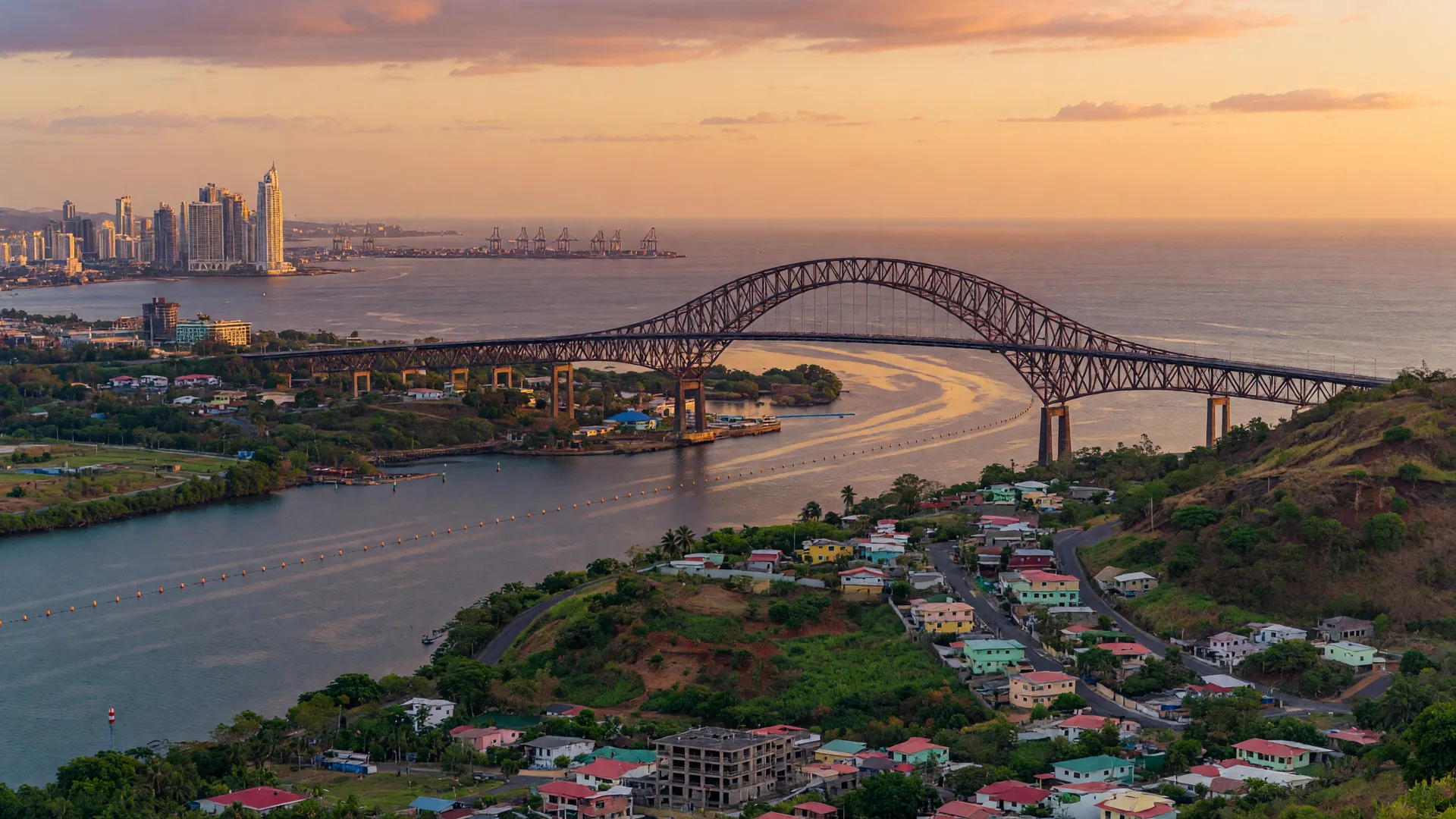 Aerial view of the Panama Canal at golden hour with the Bridge of the Americas and the developed hillsides of West Panama in the foreground