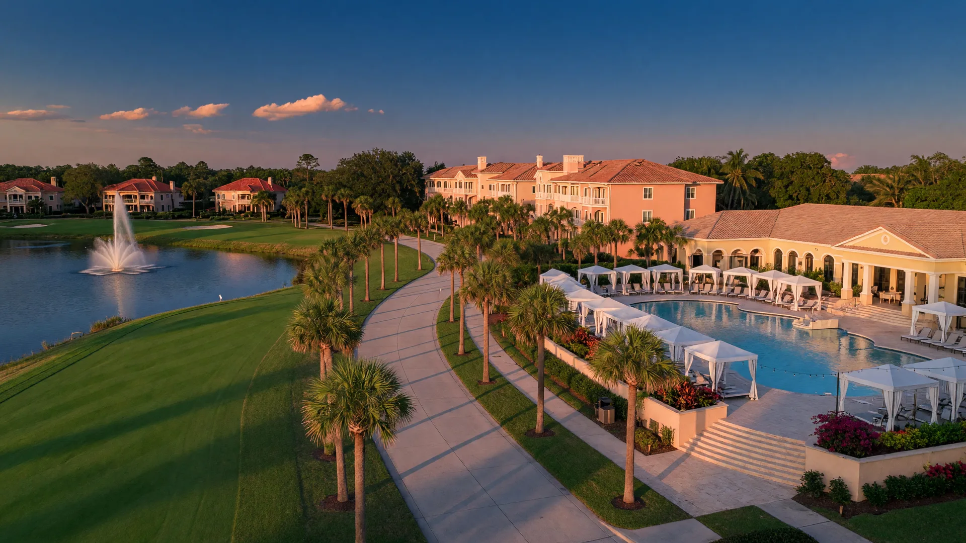 A golden-hour view of a resort-style Central Florida master-planned community: a palm-lined boulevard beside Mediterranean stucco homes, a golf fairway and fountain lake, and a community pool terrace with white cabanas.