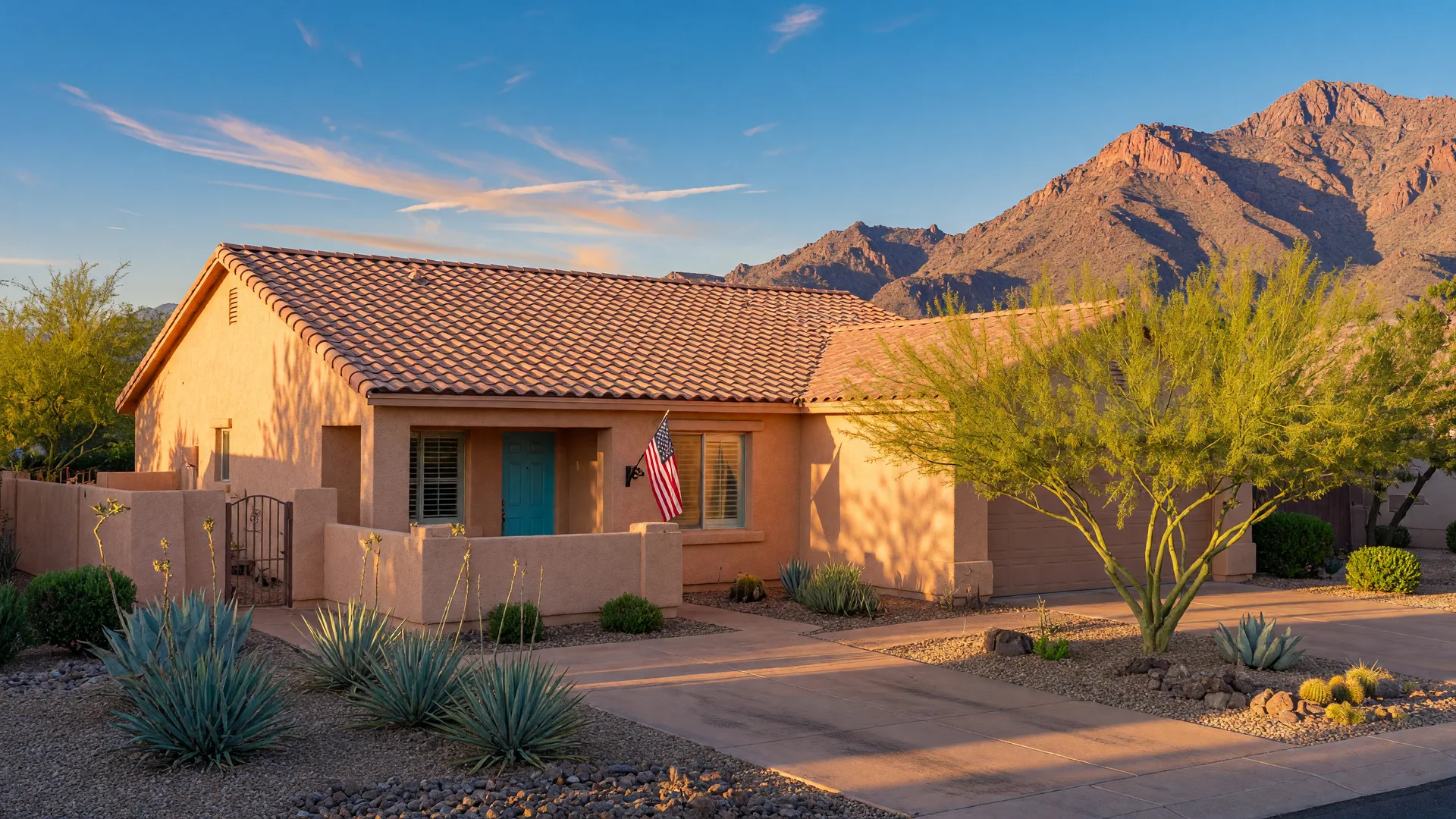 A modern Southwestern single-story home in Arizona at golden hour with a small American flag by the front door, desert landscaping, and the San Tan Mountains in the distance