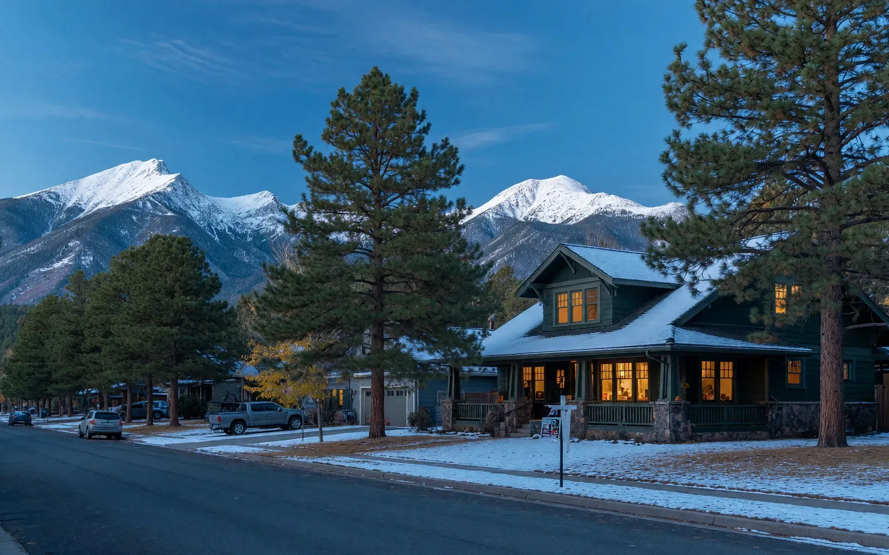 A single-family home among ponderosa pines in a Flagstaff neighborhood on a crisp late-October morning, snow dusting the roofline with the San Francisco Peaks in the distance