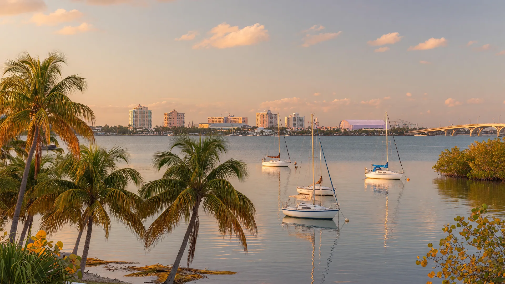 Sarasota Bay at the transition from late summer to early fall with warm amber tones, sailboats on calm water, and the Sarasota skyline in the distance
