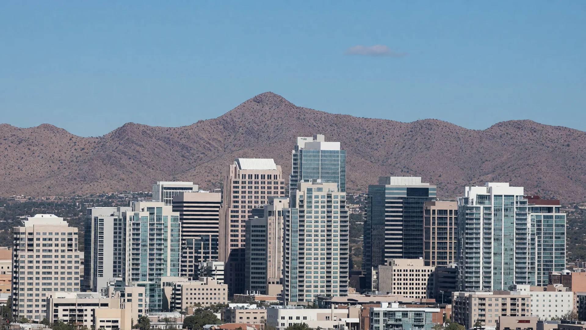 Golden hour view of downtown Phoenix with the skyline rising behind palm-lined streets and Camelback Mountain on the horizon
