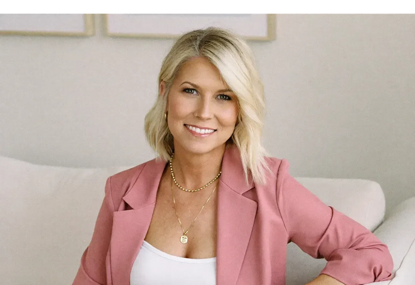 Nicole Elizabeth Yaeger in a dusty rose blazer sitting on a white sofa with an iced coffee