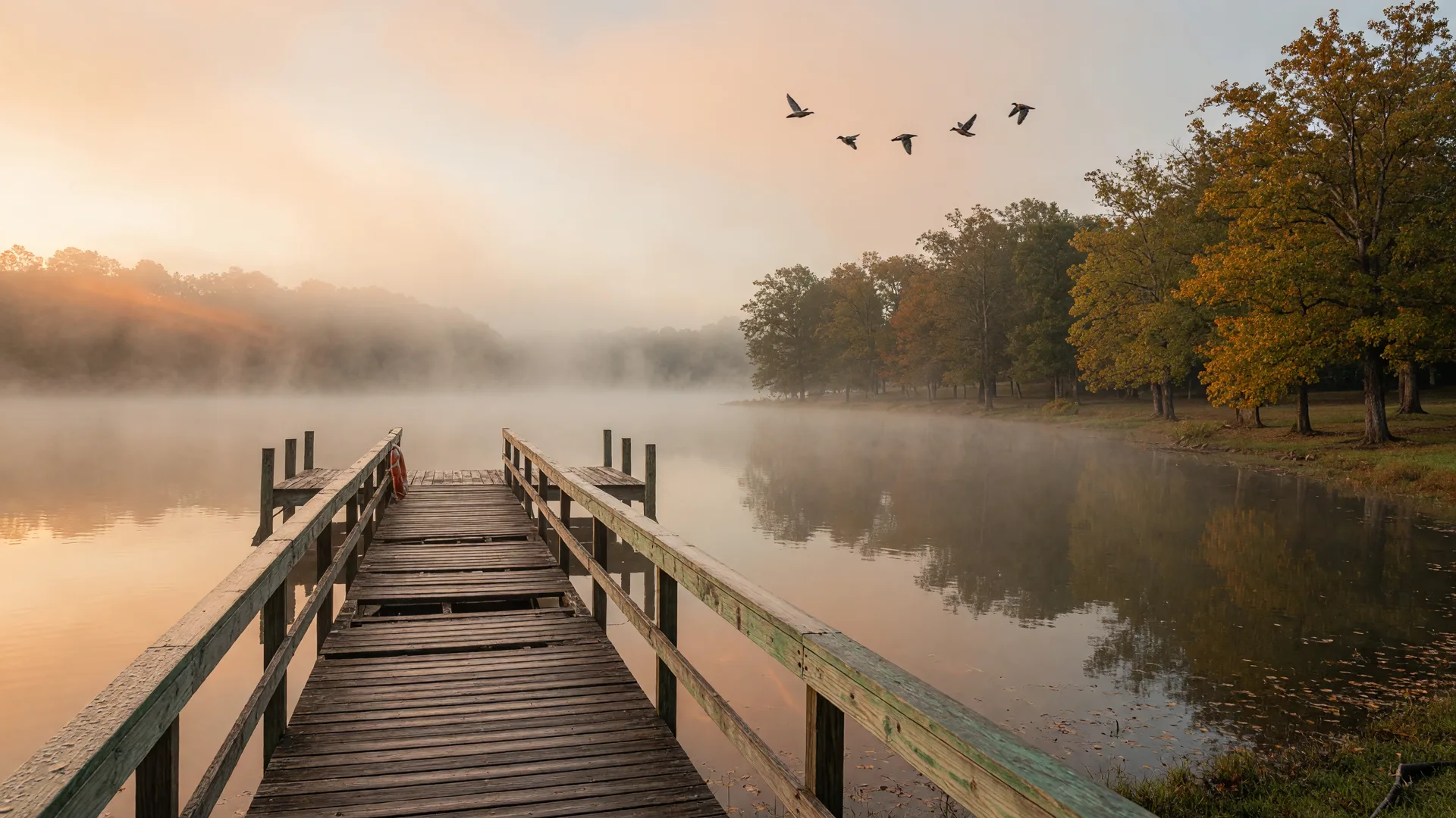 Misty early-fall morning on a Northeast Texas lake with a wooden fishing pier and amber trees at sunrise
