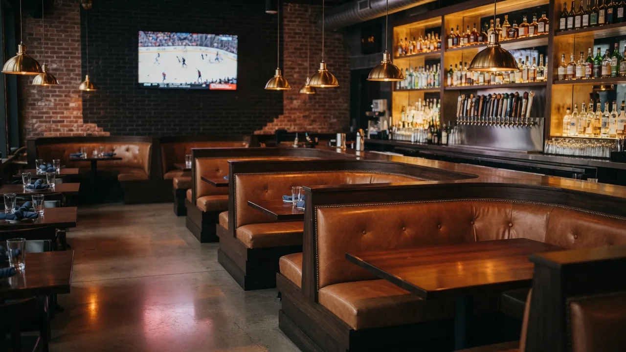 The warm wood-and-brick interior of an upscale neighborhood grill and sports bar with booths and glowing pendant lights