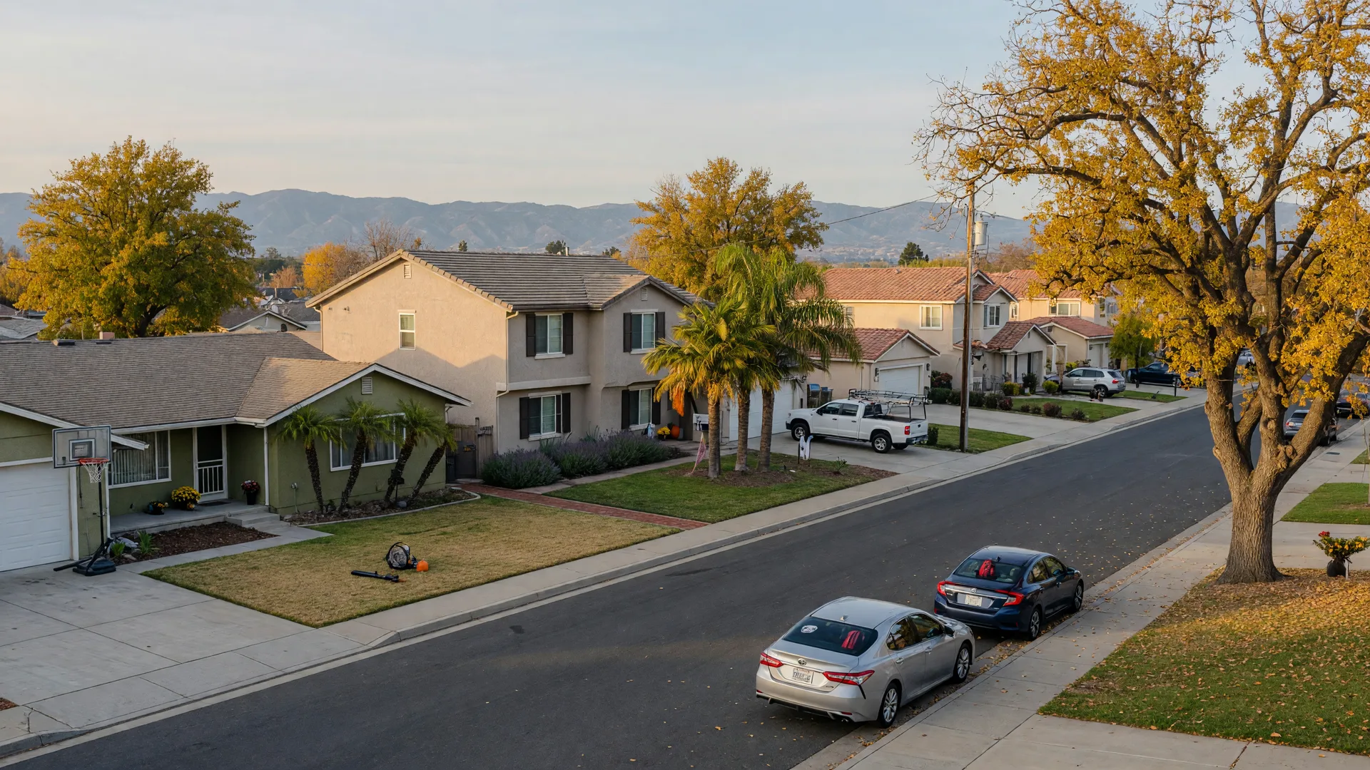 A quiet residential street in northeast Merced, California near UC Merced on a crisp October morning with ranch and newer tract homes, neat lawns, mature oak and palm trees, and the Sierra Nevada foothills on the horizon