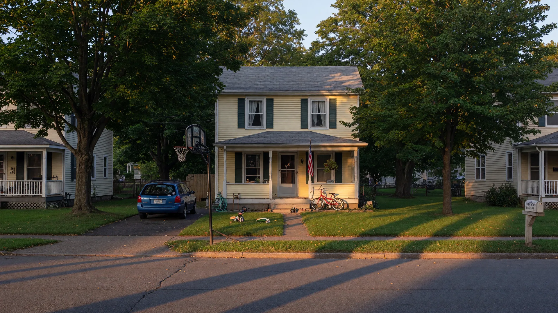 A quiet suburban family home on a late summer afternoon with a bicycle leaning against the front porch and mature trees casting long shadows