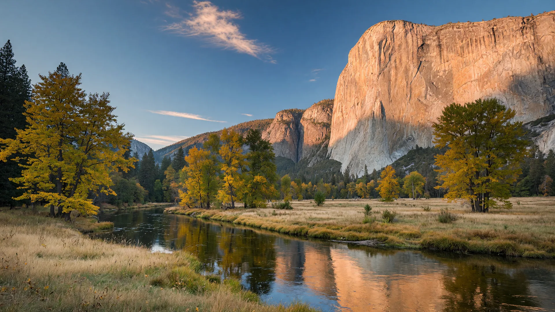 The Merced River in Yosemite Valley in early October at golden hour, cottonwoods and bigleaf maples just beginning to turn gold and amber along the water, El Capitan glowing in late afternoon light
