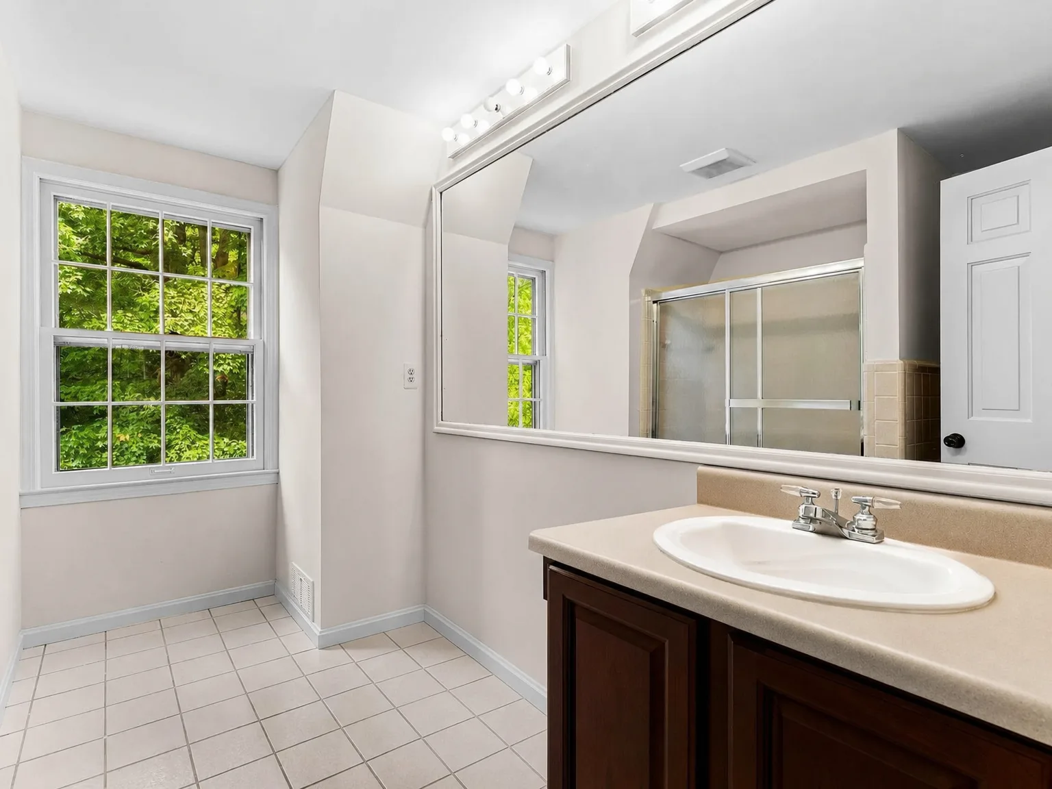 Bathroom with dark wood vanity, large mirror, and natural light from the window