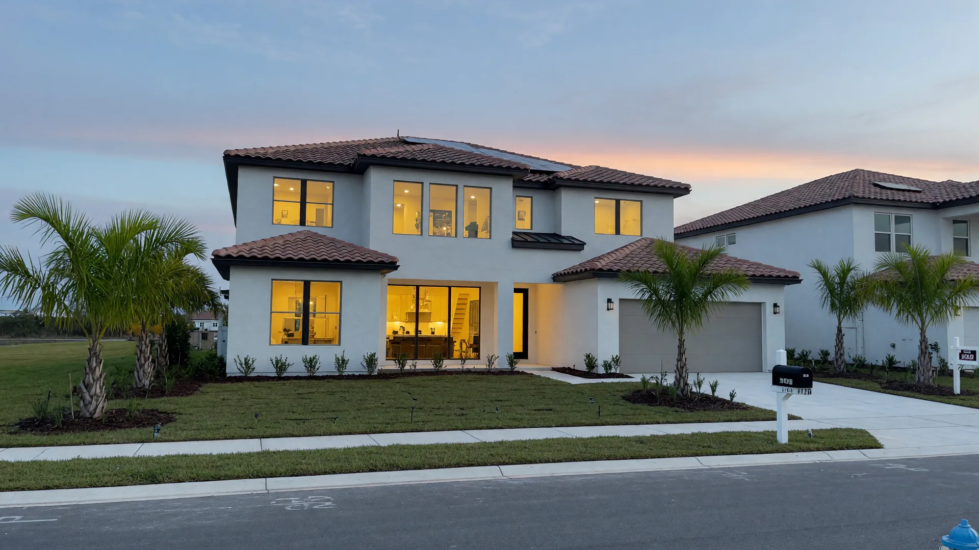 A modern Central Florida new-construction home at dusk, with a tile roof, warm glowing windows, and palm trees, seen from the street.