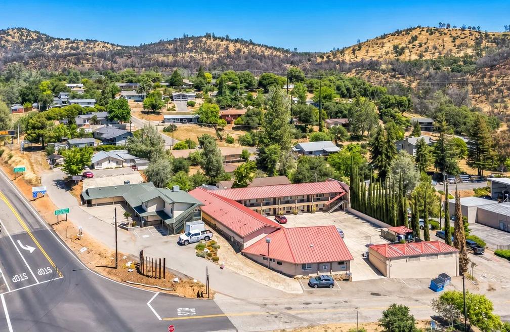 The historic red-roofed motel complex in Mariposa, California set against golden hills and a blue sky