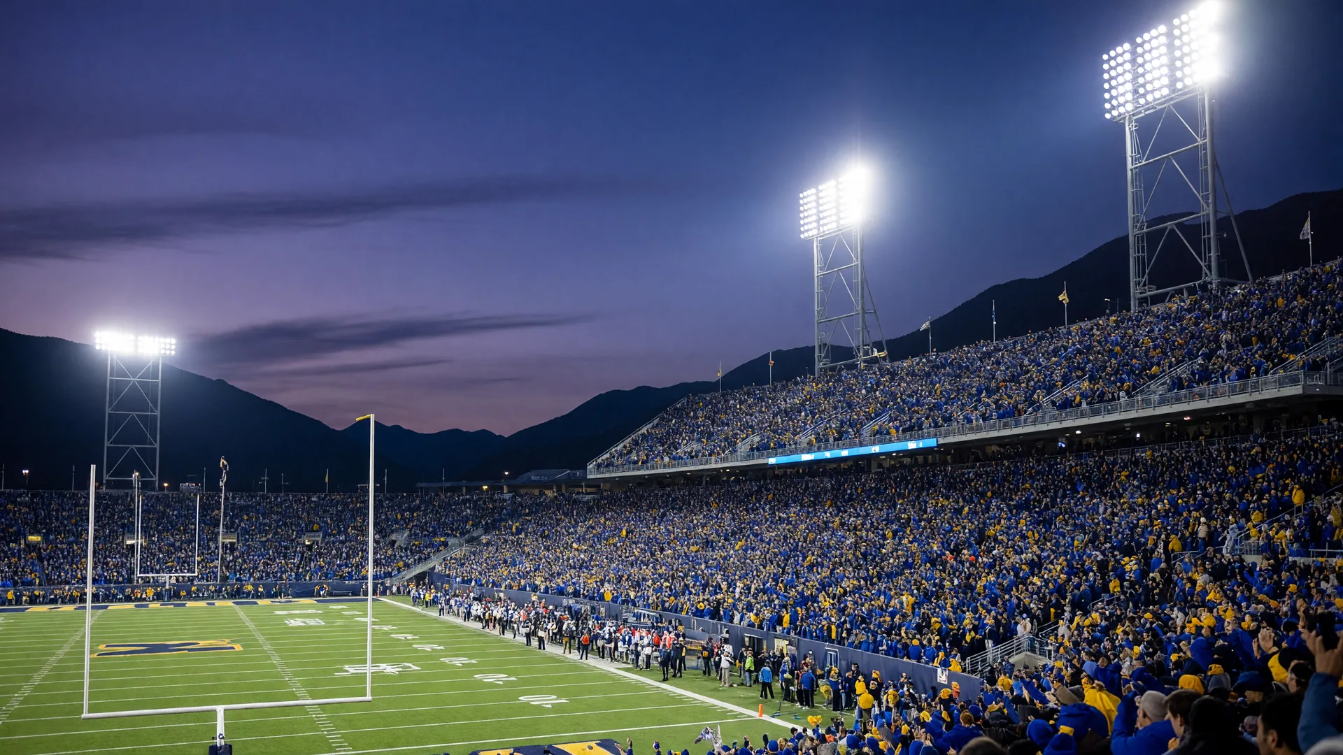 A packed college football stadium at night under bright floodlights seen from a low end-zone angle