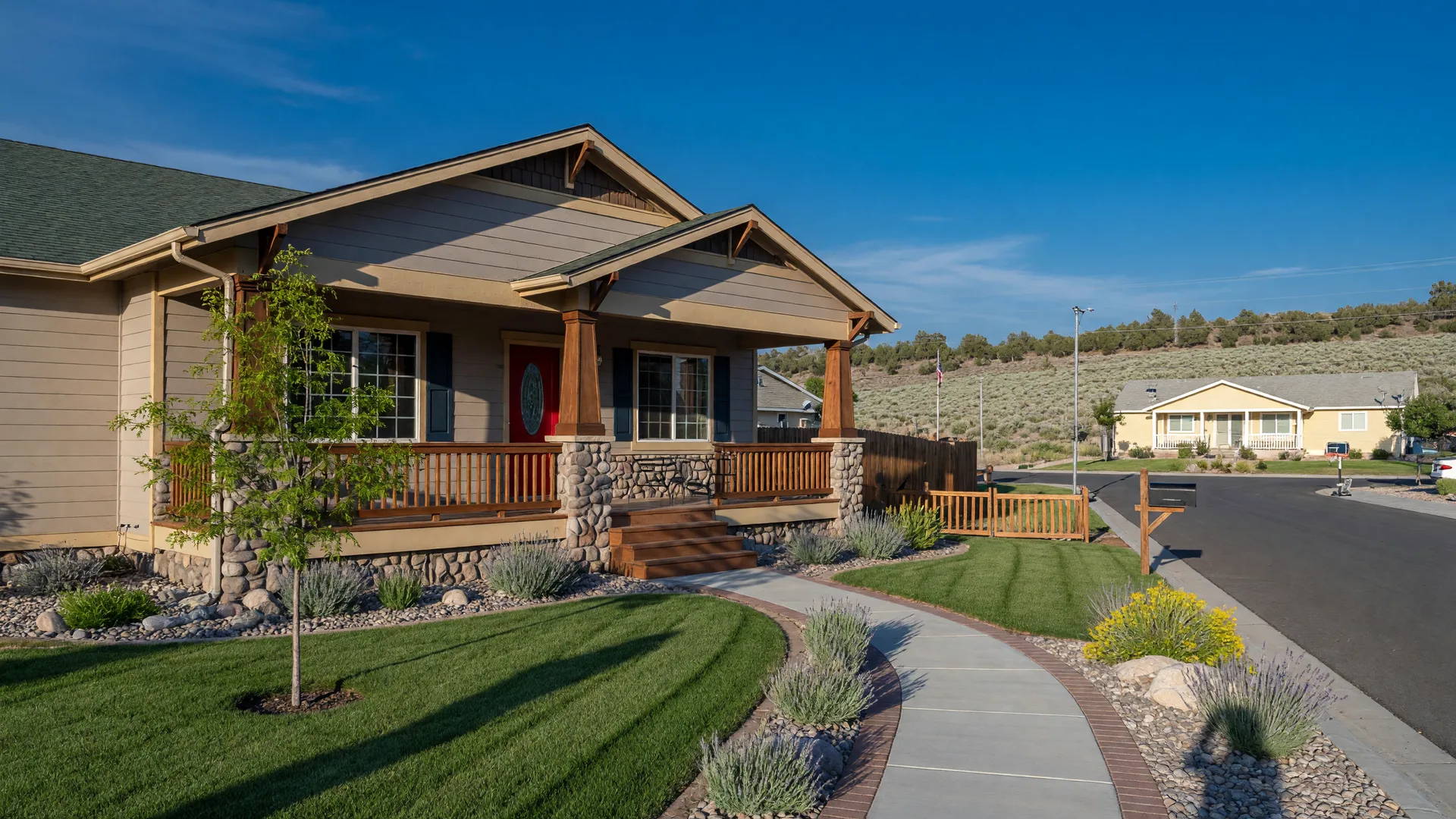 A comfortable mid-size suburban Nevada home on a bright morning with a tidy yard, a young tree, and a second smaller home visible down the street.