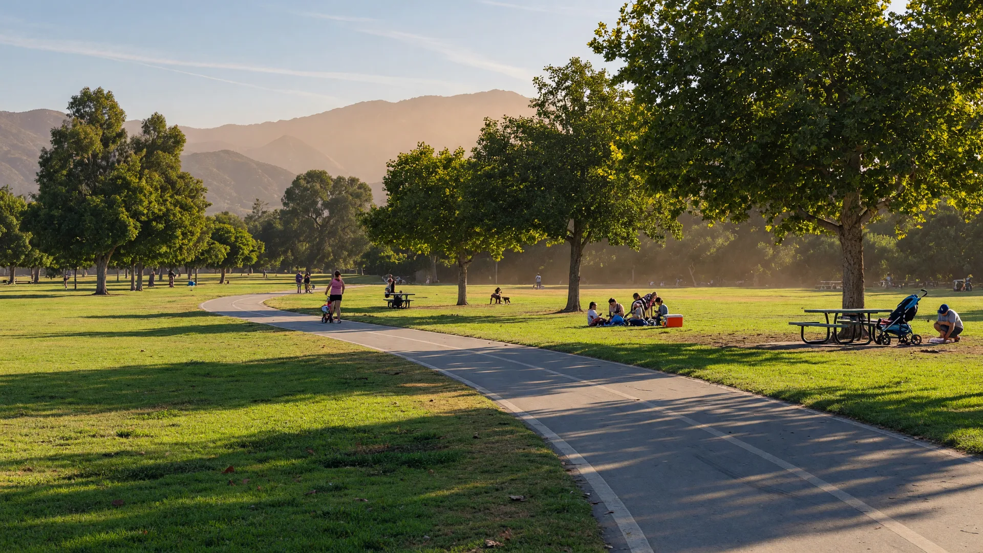 Sunny Southern California community park with a walking trail, mature shade trees, and distant mountains