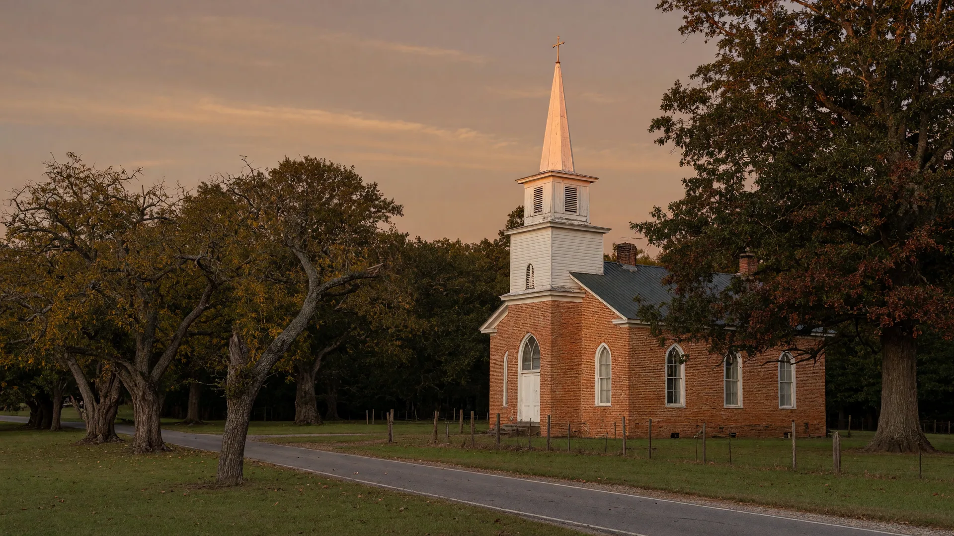A small historic brick country church with a white steeple at dusk on a tree-lined northeast Georgia lane