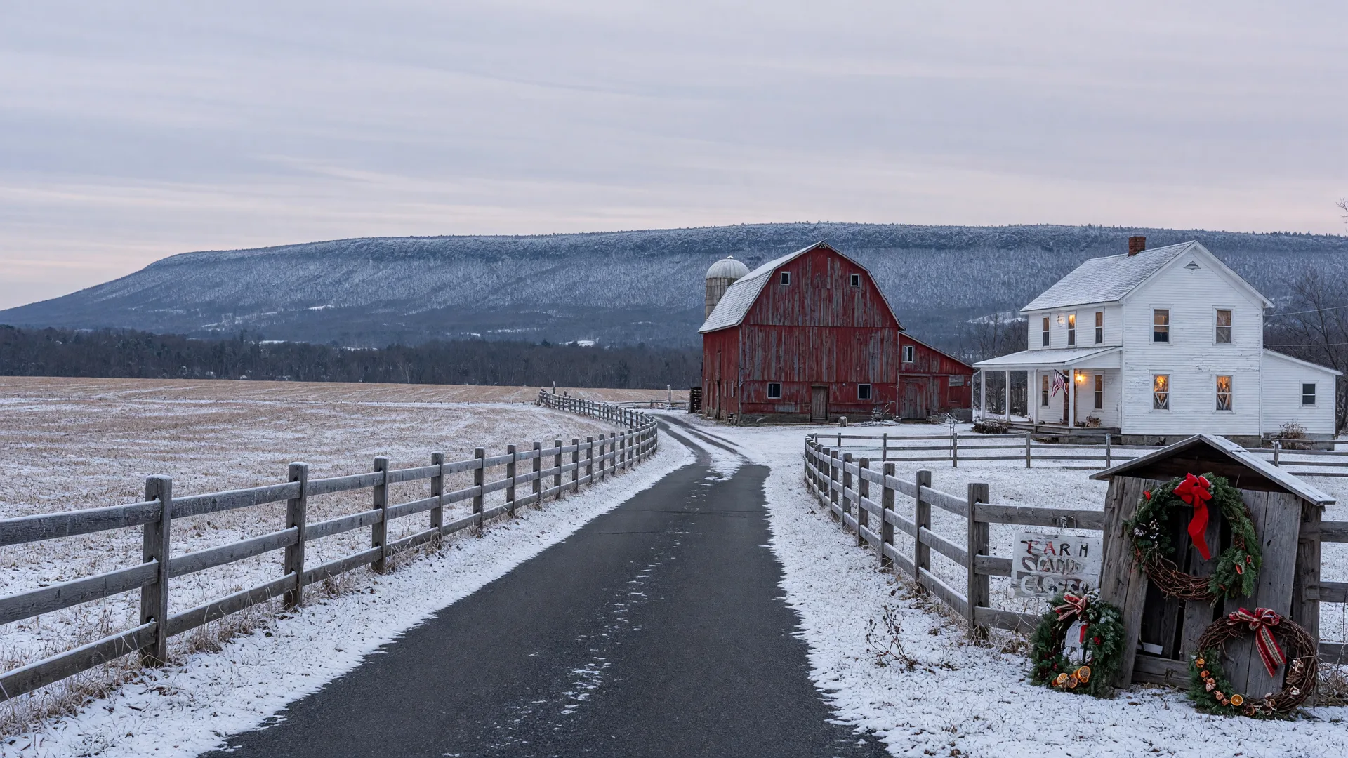 A quiet Lehigh Valley country lane in early December with a light dusting of snow, a red barn and white farmhouse with warm glowing windows, holiday wreaths on a farm stand, and the snow-dusted Blue Mountain ridge on the horizon