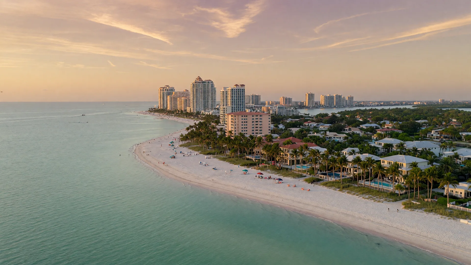 Aerial view of the Southwest Florida Gulf coast with the Naples skyline in the distance, turquoise water, white sand beaches, and palm-lined shoreline