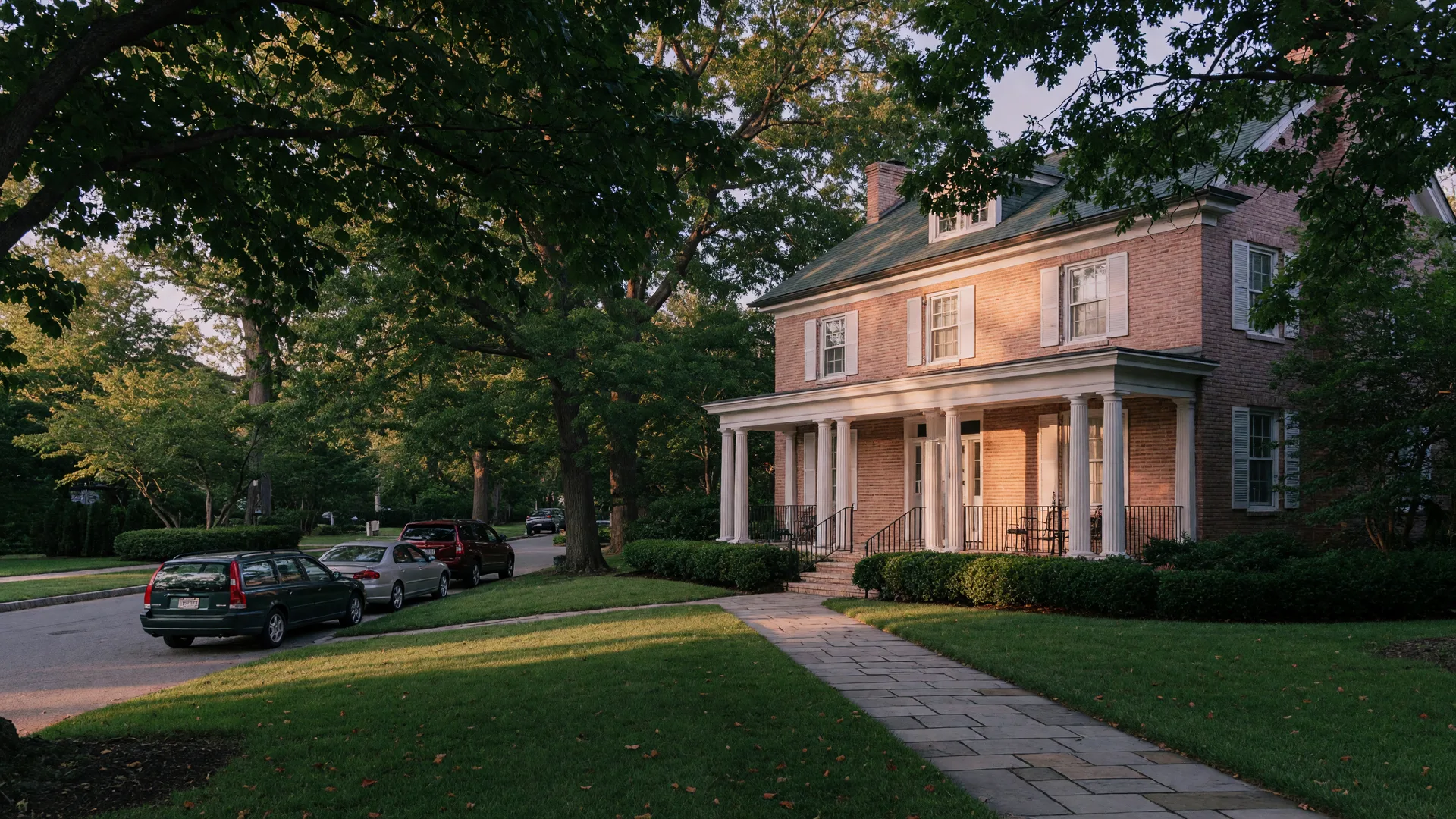 A stately Colonial Revival brick home on a leafy Chevy Chase village street in warm evening light