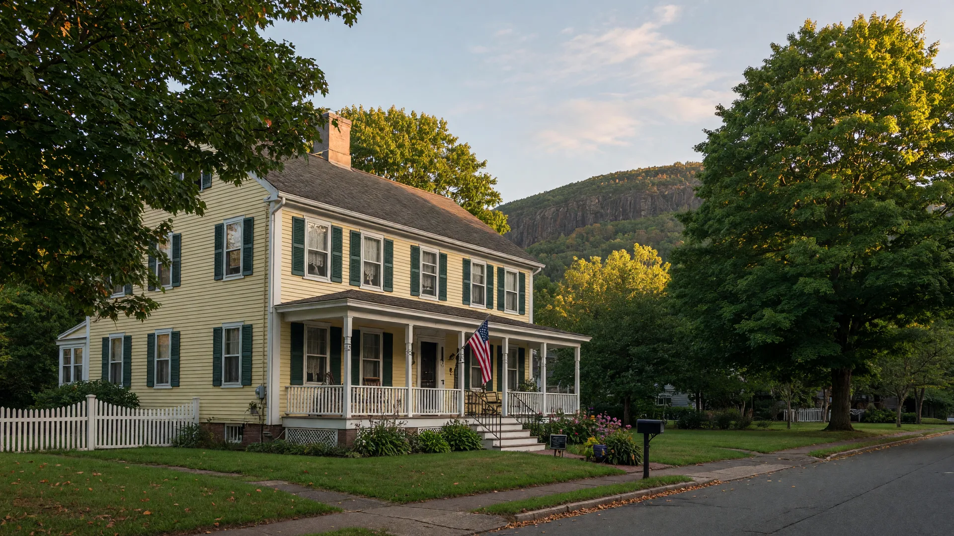 A stately century-old colonial home with dark shutters and a porch set on a tree-lined East Rock street beneath the traprock ridge
