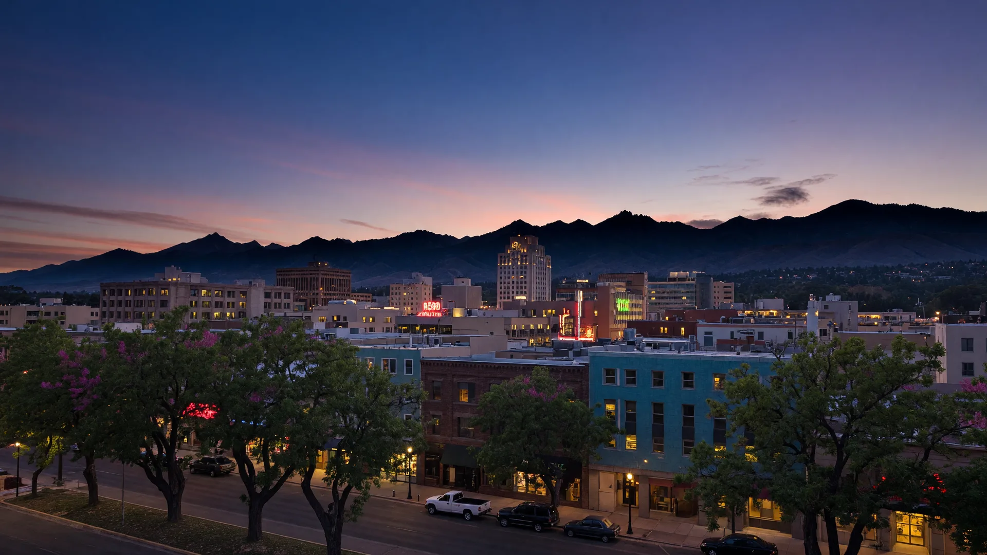Downtown Reno at dusk with the low-rise skyline glowing with warm lights and the darkening Sierra Nevada range on the horizon.