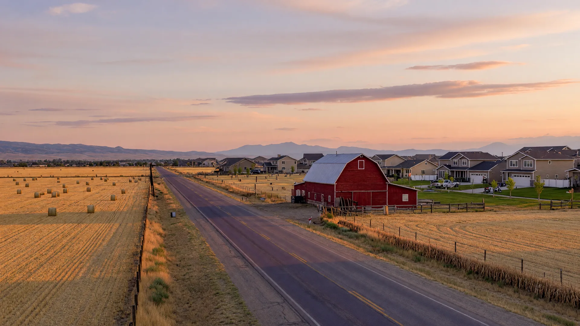 Country road with a red barn and hayfields near Kuna, Idaho at sunset with mountains in the distance