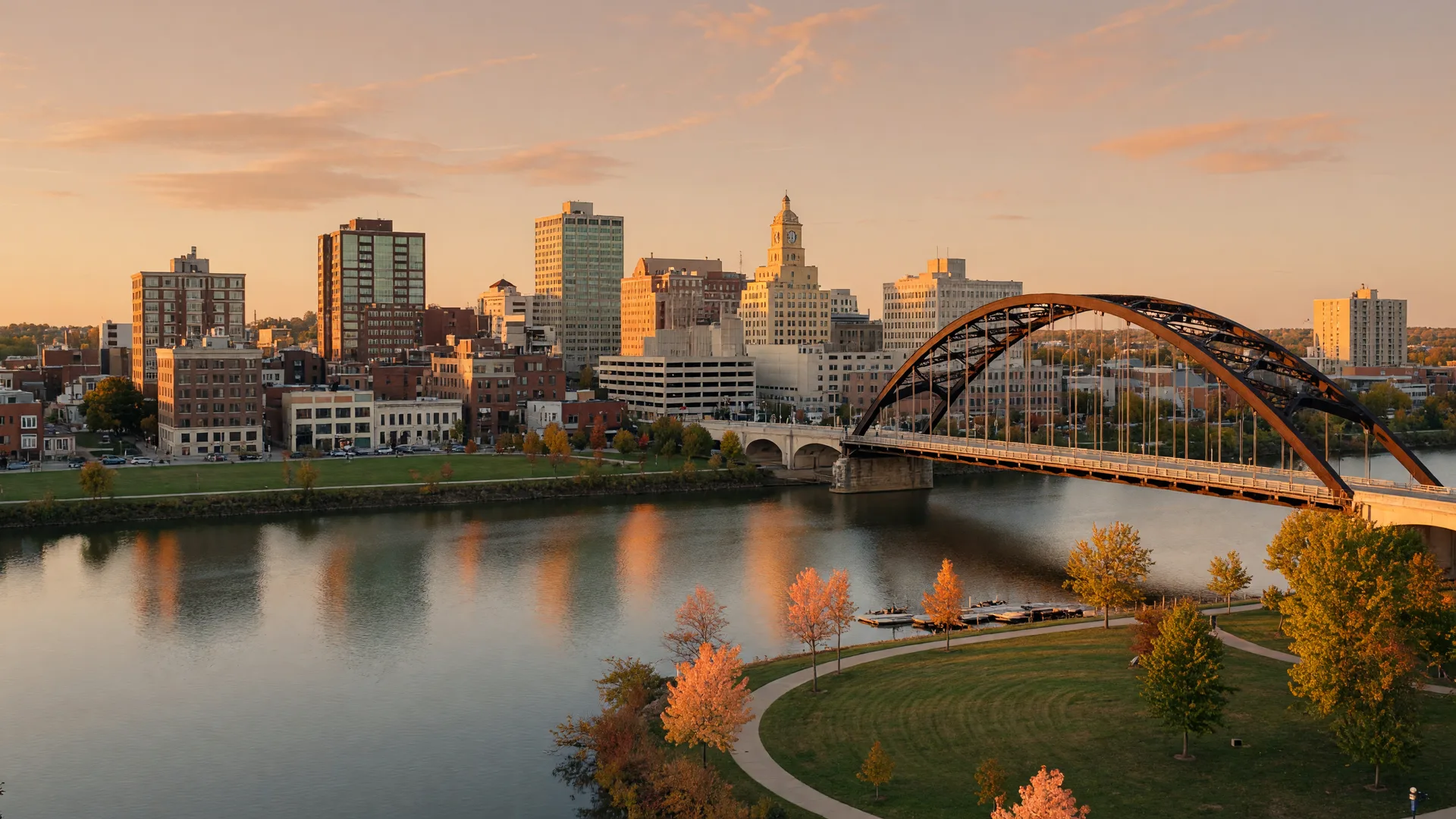 The Peoria, Illinois skyline along the Illinois River at golden hour, with a steel arch bridge and warm reflected light on the water