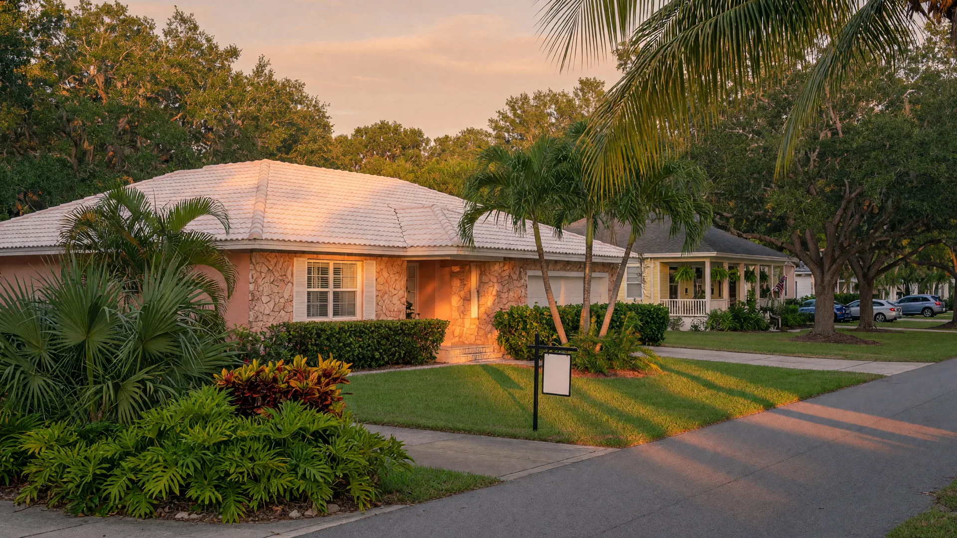 A well-kept Florida home on a tree-lined Tampa Bay street at golden hour with a For Sale sign on the front lawn