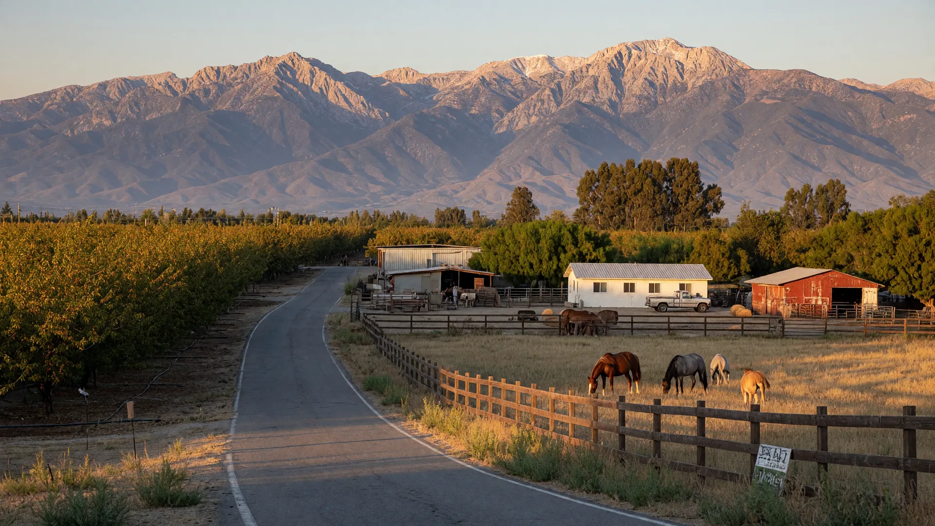 Country lane in Cherry Valley lined with orchards and ranch properties, horses in a pasture, and the San Bernardino Mountains behind