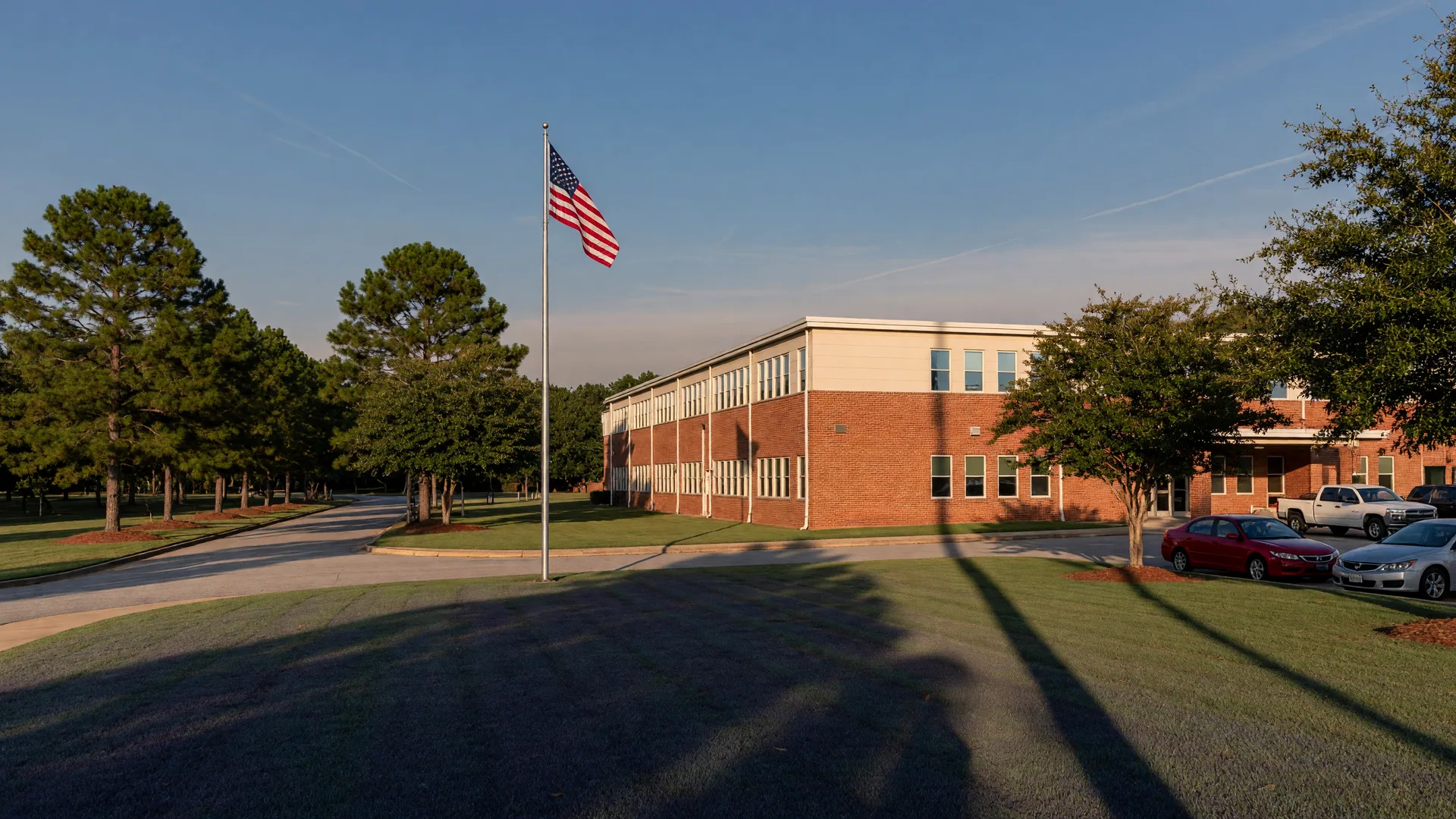 Suburban public high school campus in DeKalb County with a two-story brick and siding building, flagpole, green lawns, and southern pines