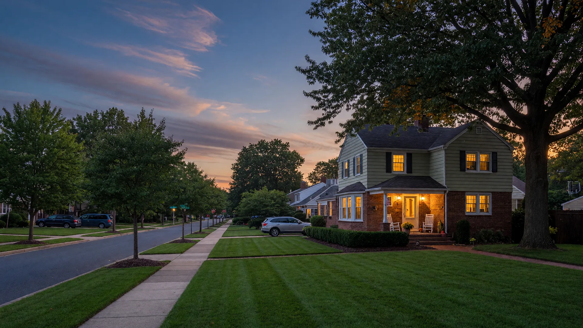 A well-kept suburban single-family home in the Philadelphia suburbs at dusk, warm light glowing from the windows under a deep blue twilight sky