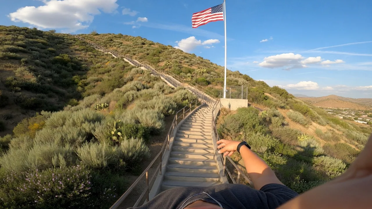 Selfie at the flagpole at the top of the SCV Stairs in Santa Clarita with the American flag waving against a bright blue sky.