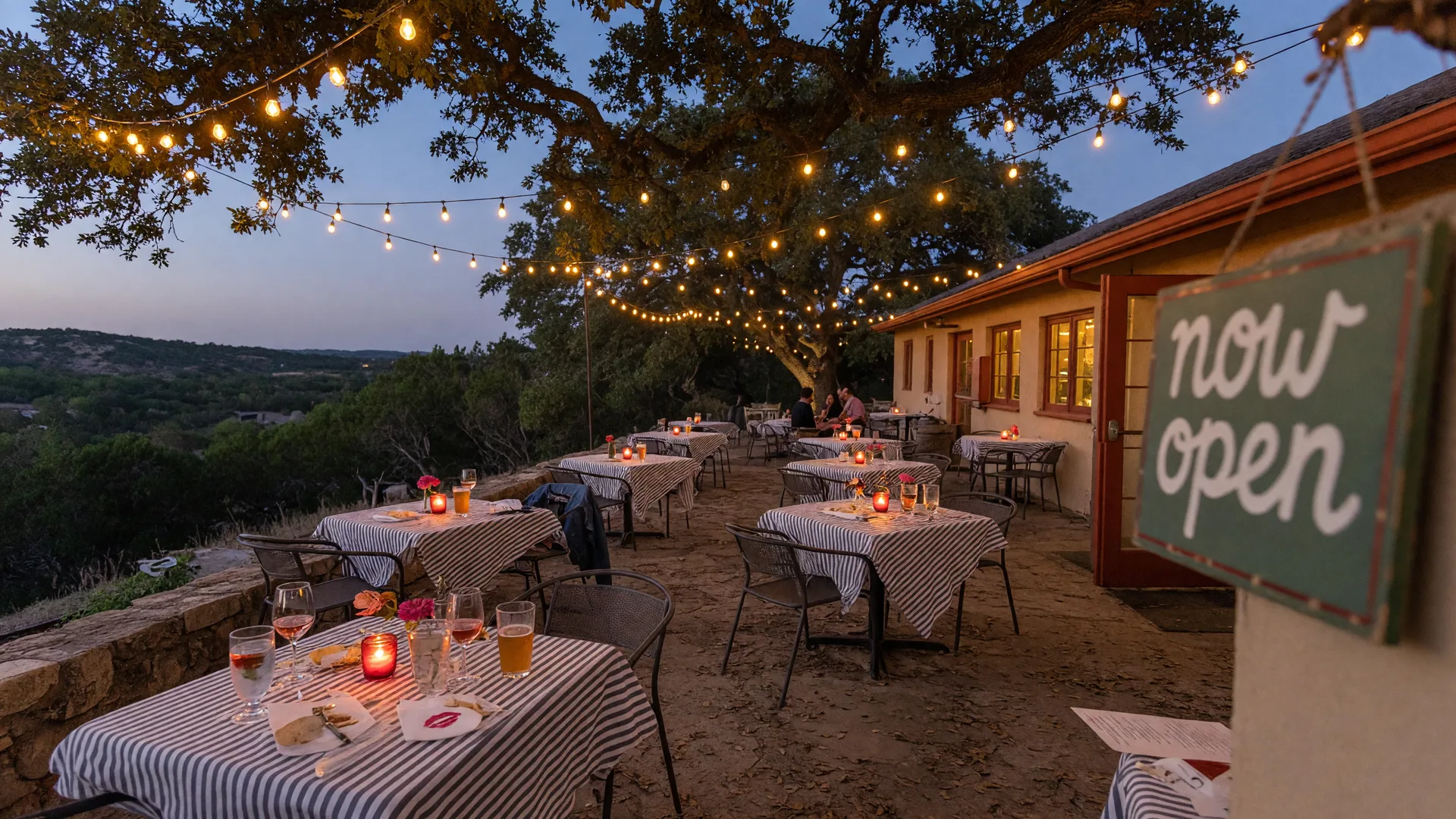 A new restaurant patio in the Texas Hill Country at dusk with warm string lights over live oaks and candlelit bistro tables