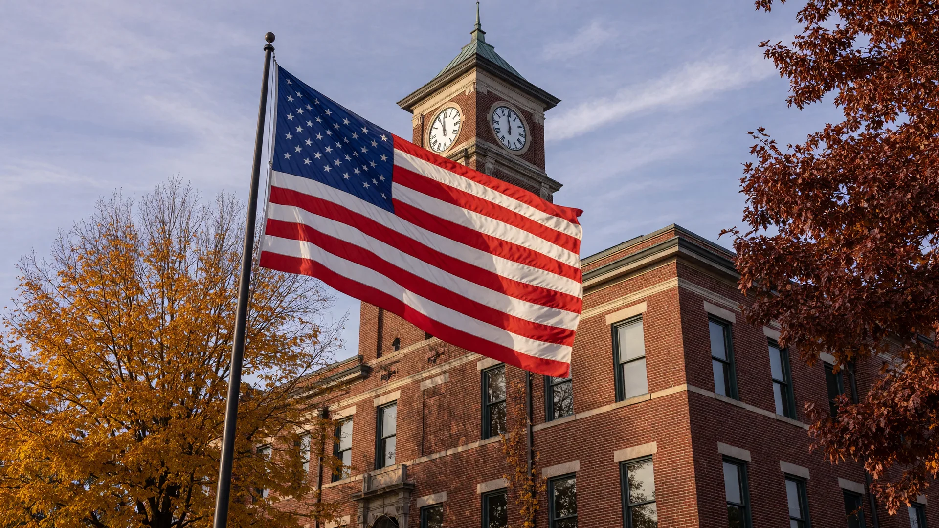 An American flag rippling in the wind in front of a red-brick Ohio city hall on a crisp November morning with autumn trees