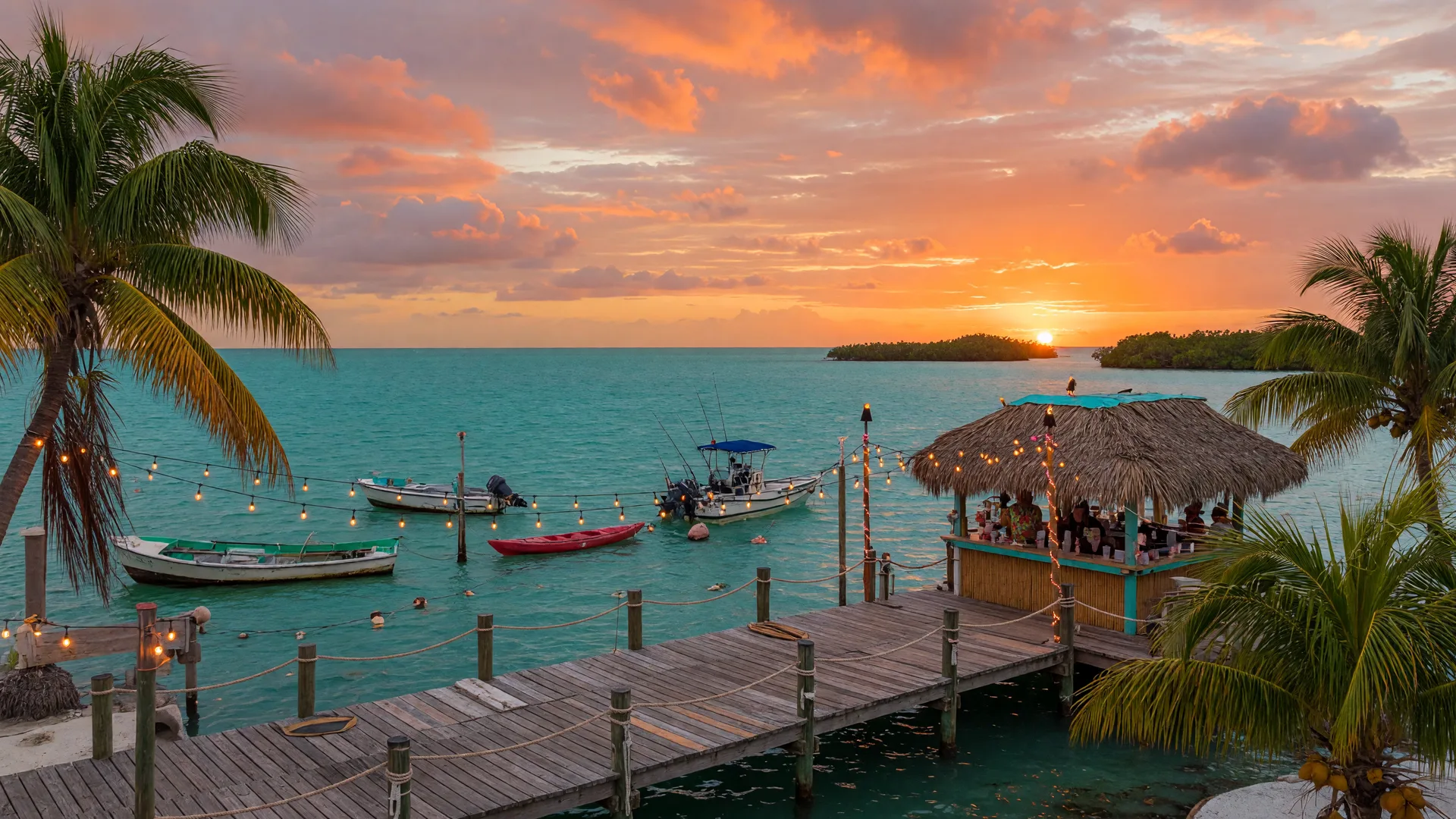 Florida Keys tiki bar and dock at golden hour with string lights and palm trees framing a spectacular sunset over turquoise water
