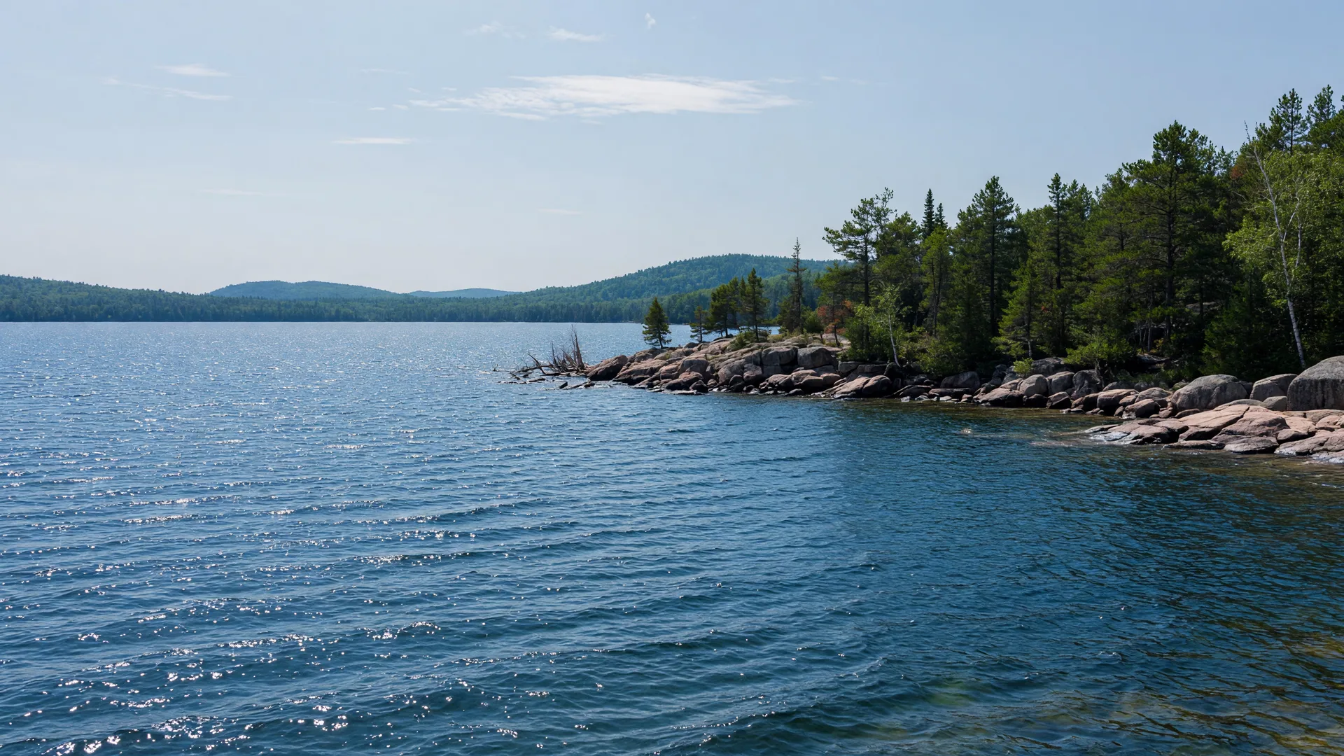 Deep, clear northern Minnesota lake in bright summer light with a rocky, pine-fringed point