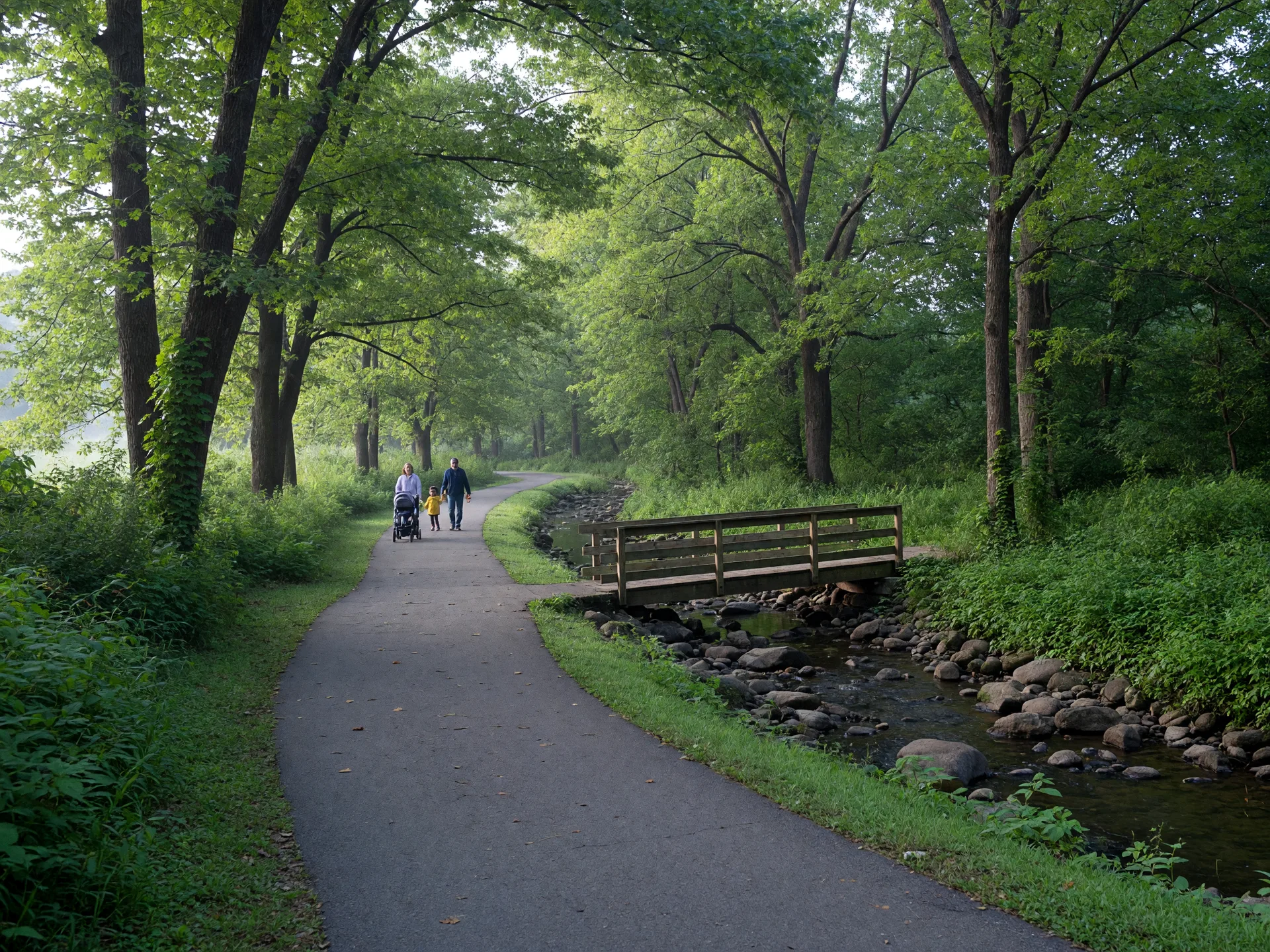 A paved trail winding beside Sligo Creek with a wooden footbridge and tall shade trees