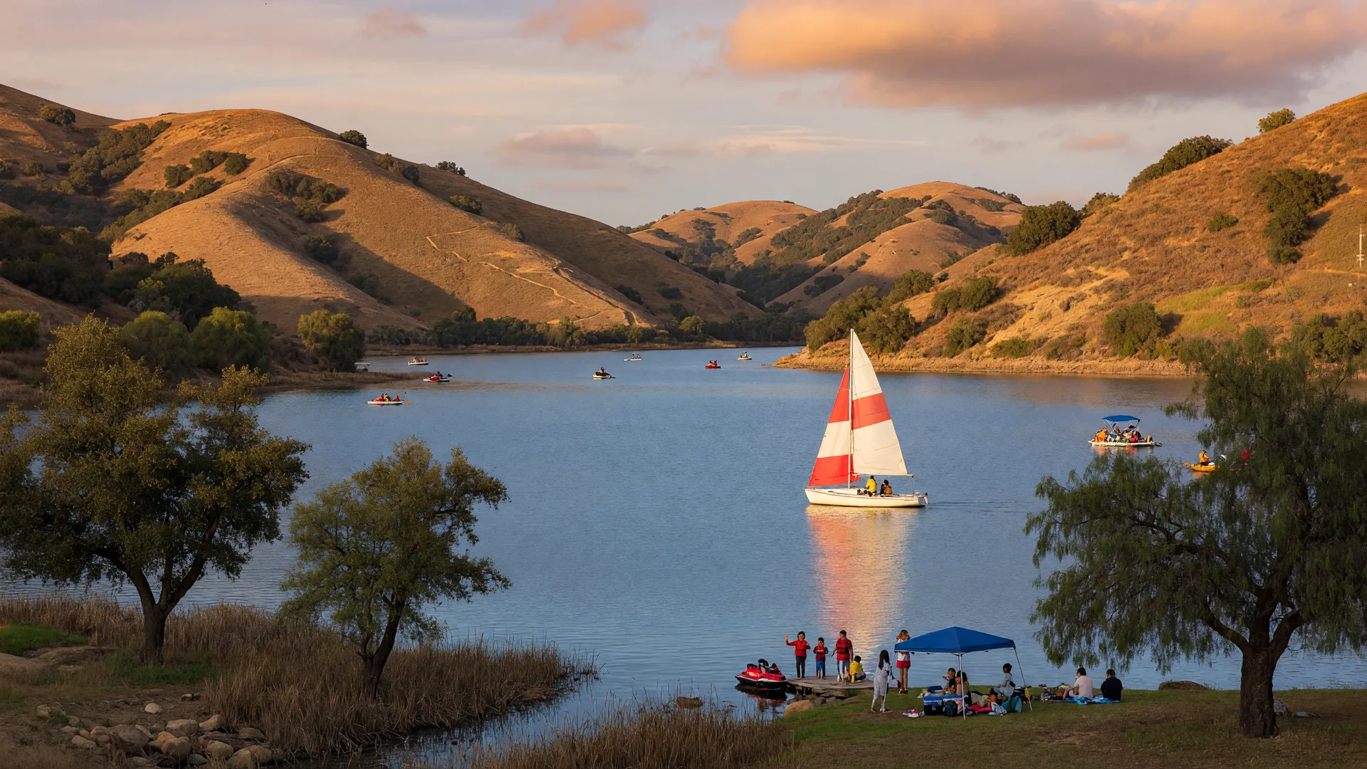 Castaic Lake at golden hour with sailboat on calm water surrounded by golden hills