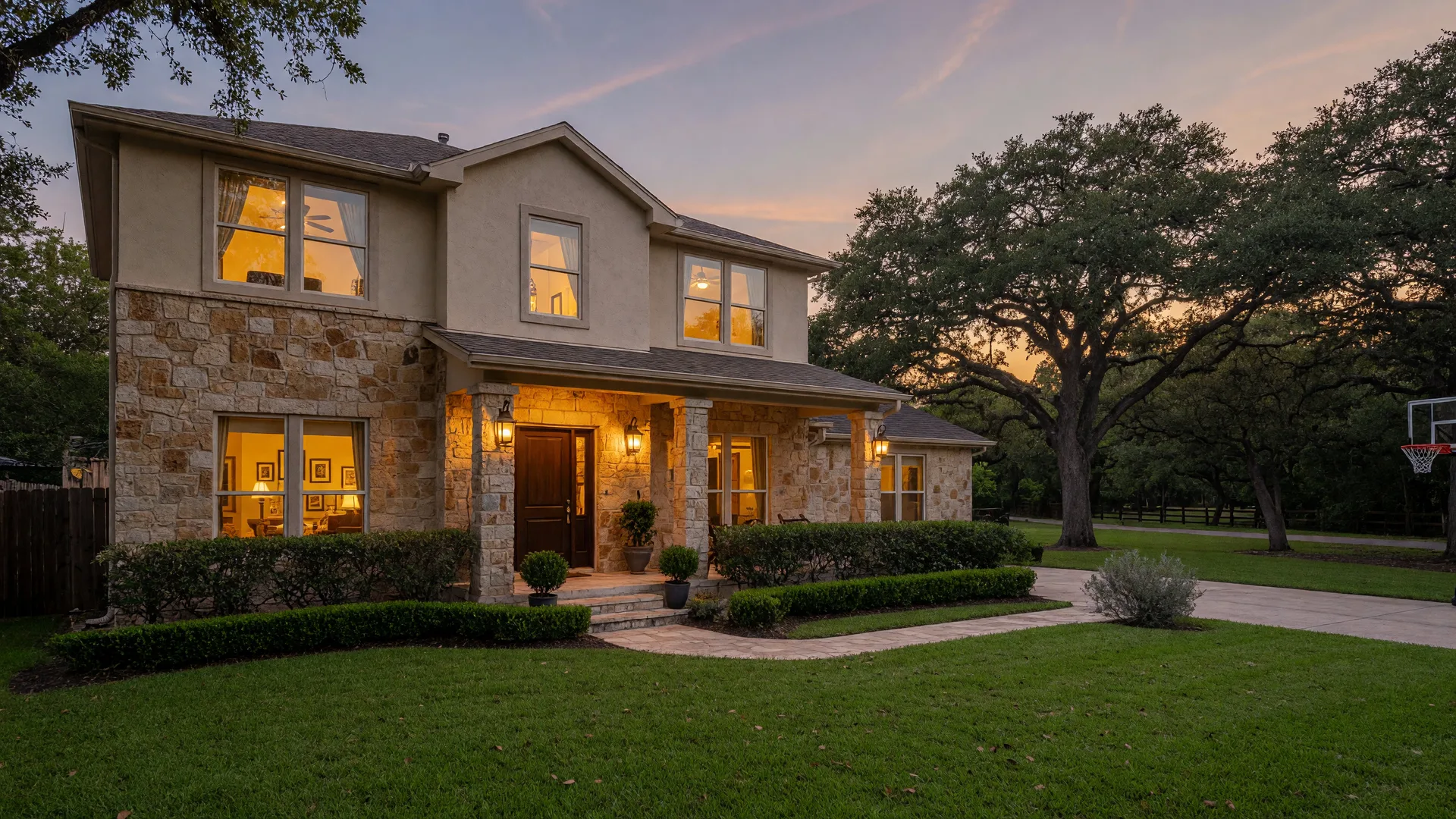 Modern stone-and-stucco family home in Stone Oak, a family-friendly San Antonio real estate community, at dusk with a greenbelt behind it