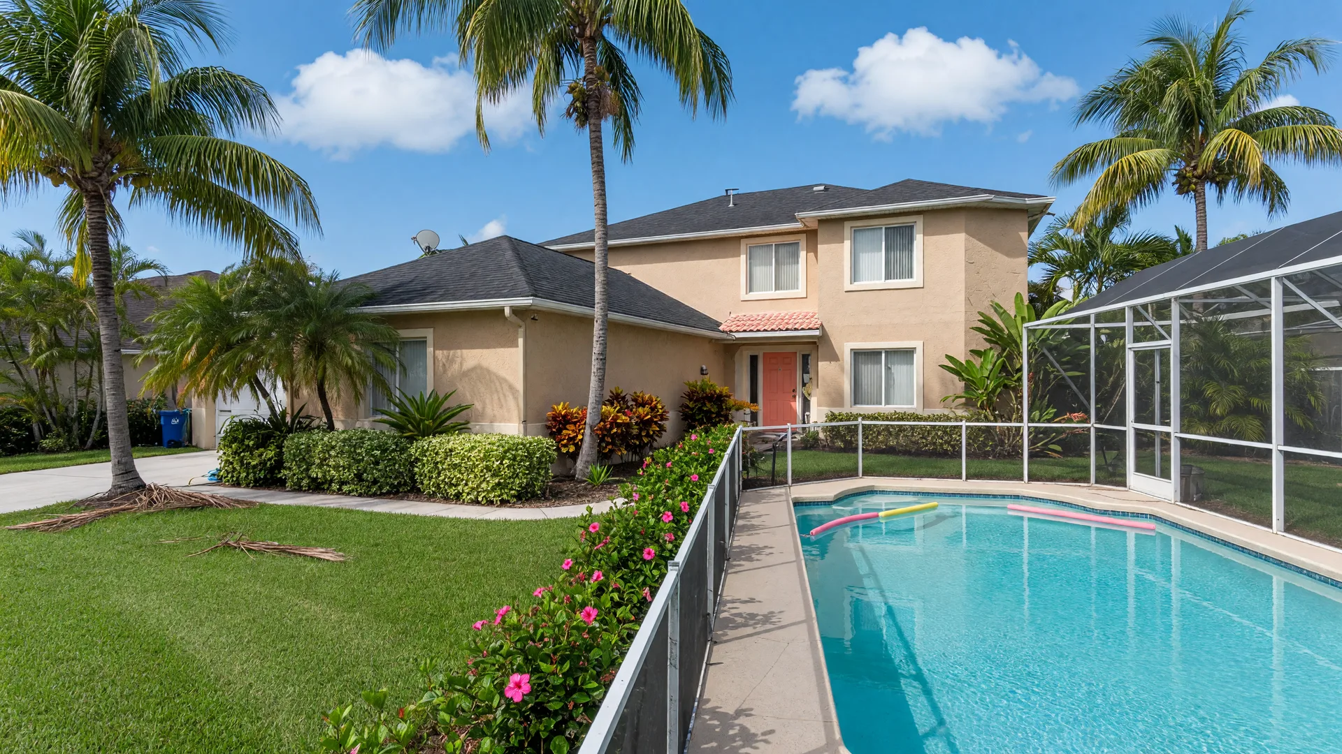 A sunlit suburban Florida home with a screened pool, palm trees, and tropical landscaping under a blue sky.