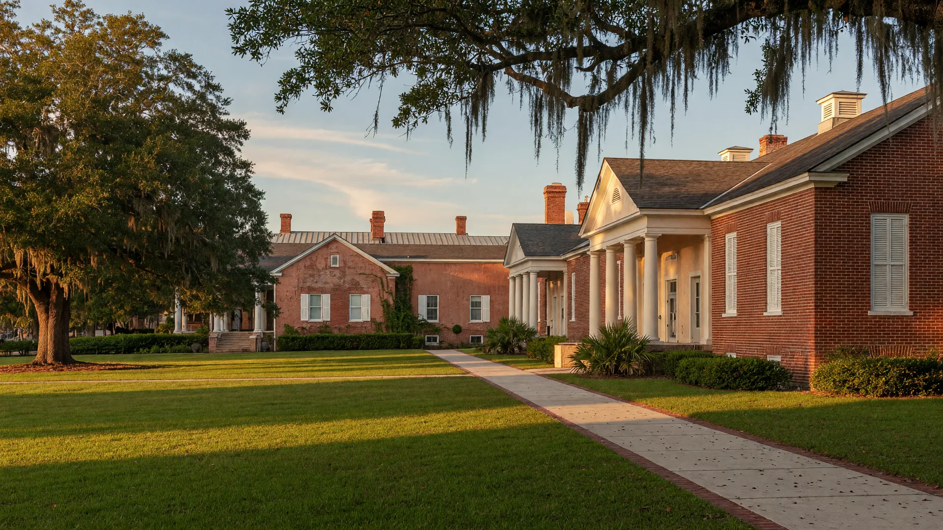School campus with brick classroom buildings and white columns framed by moss-draped live oak trees