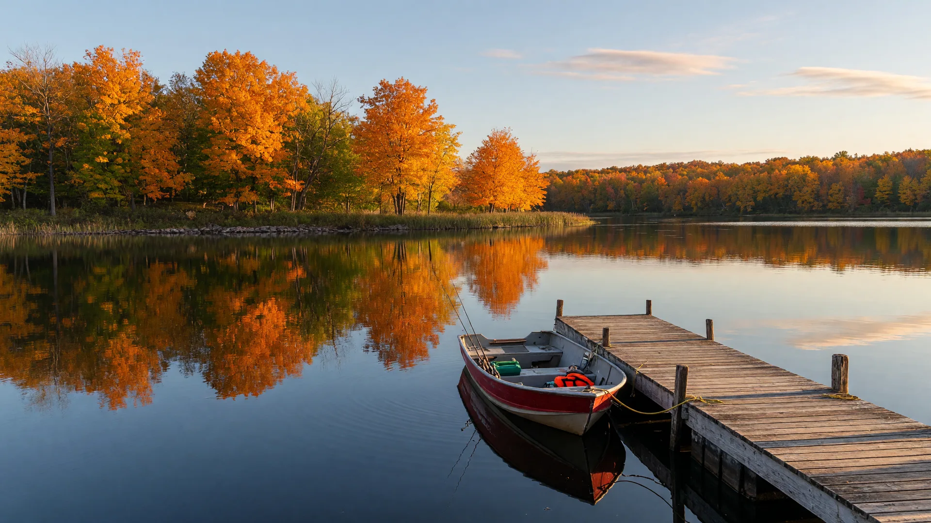 A Minnesota lake in early autumn with a wooden dock and a small fishing boat, calm water reflecting orange and gold shoreline