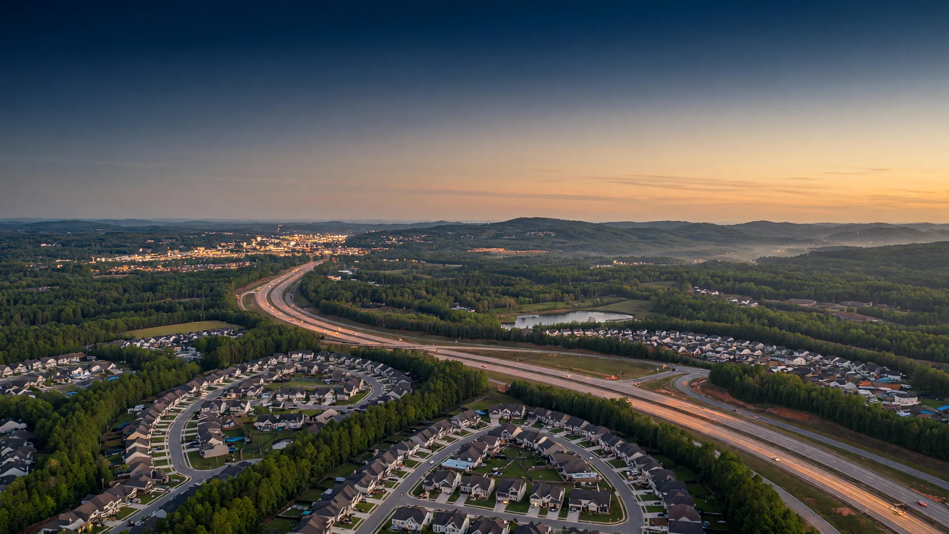 Aerial dusk view of a residential suburb in north Gwinnett County, Georgia, with an interstate curving through forested hills