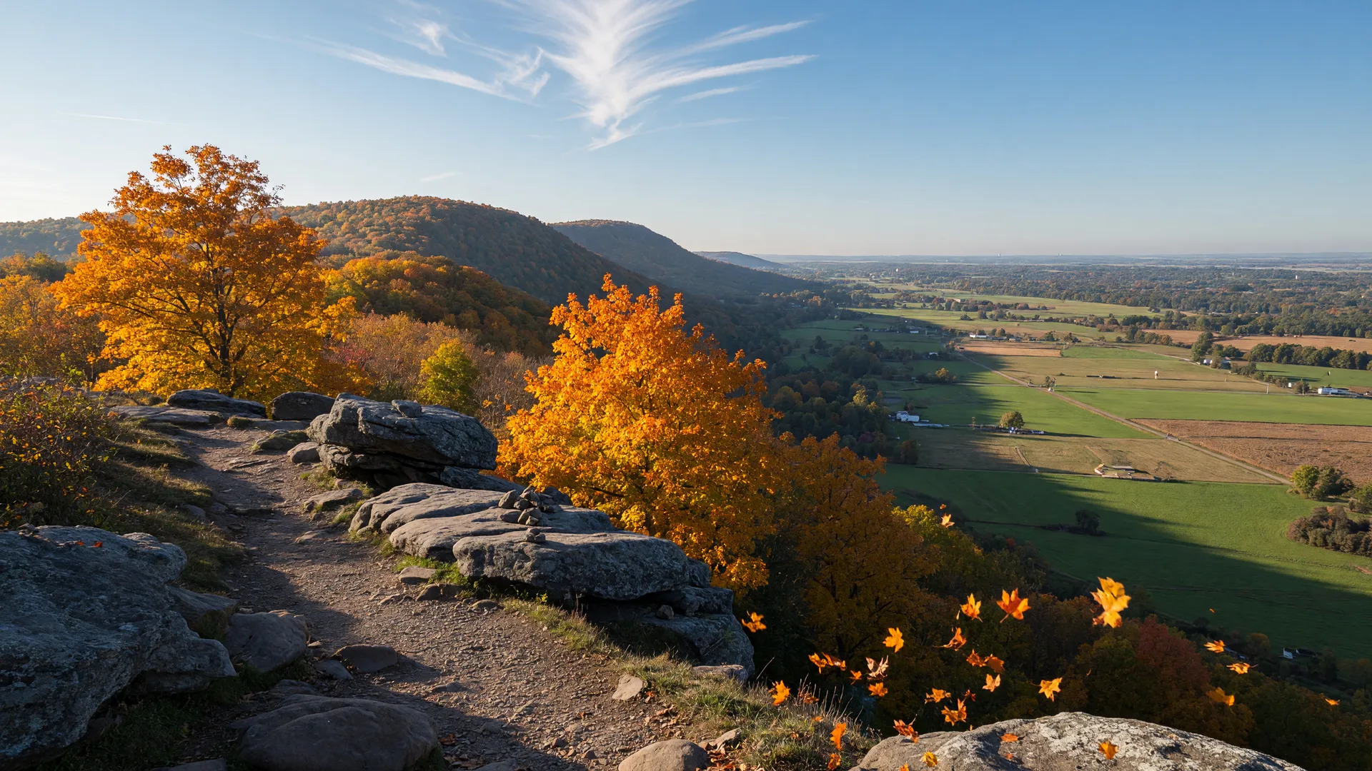 A crisp mid-October morning view from a rocky Blue Mountain ridge overlook in Lehigh County, with the Appalachian Trail winding through gold and orange sugar maples on the ridgeline and the valley floor still mostly green below